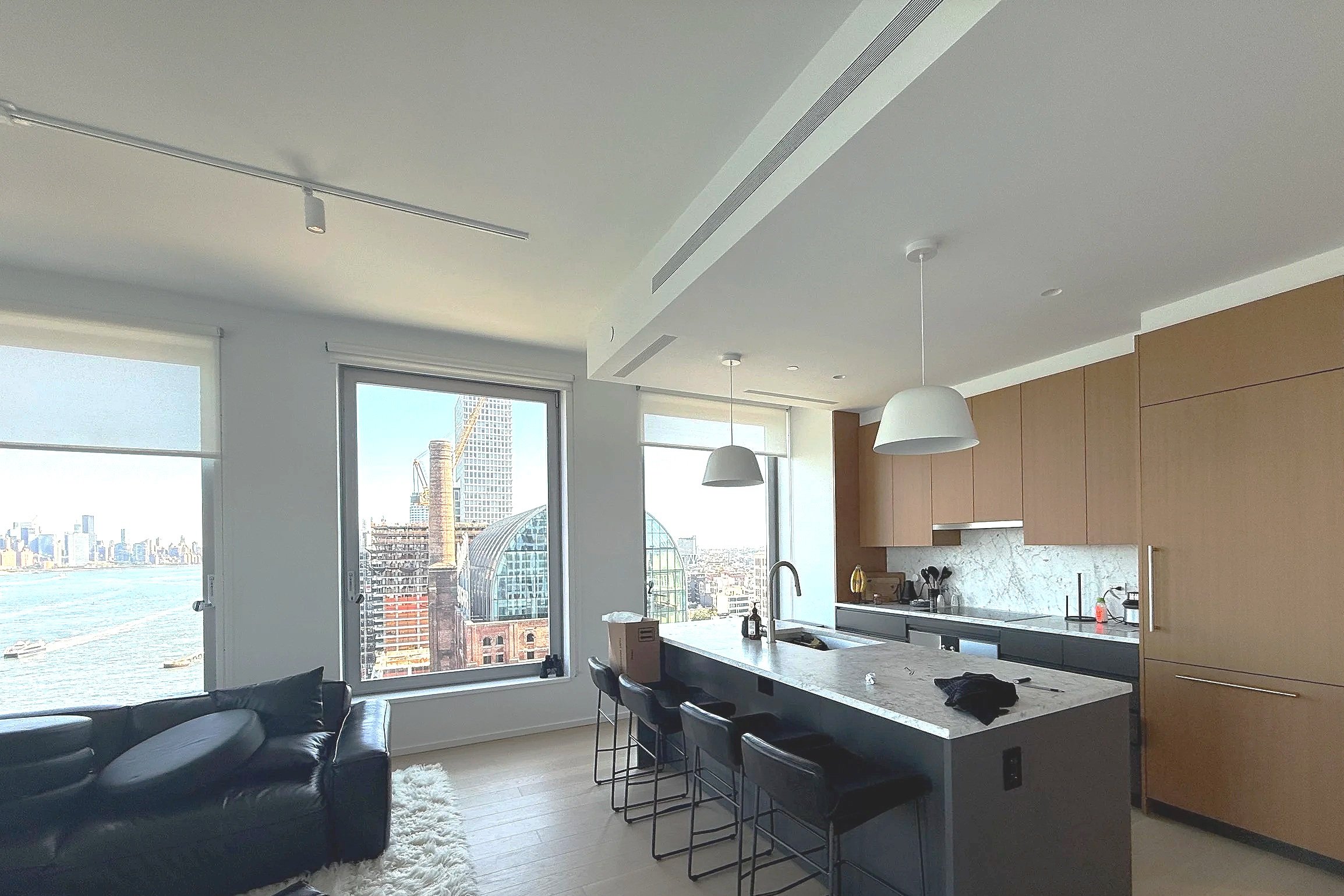 Photo of an unpainted apartment building overlooking Williamsburg Brooklyn's former Domino Sugar Factory buildings, featuring white walls and ceilings and a mix of dark and light grey cabinets.