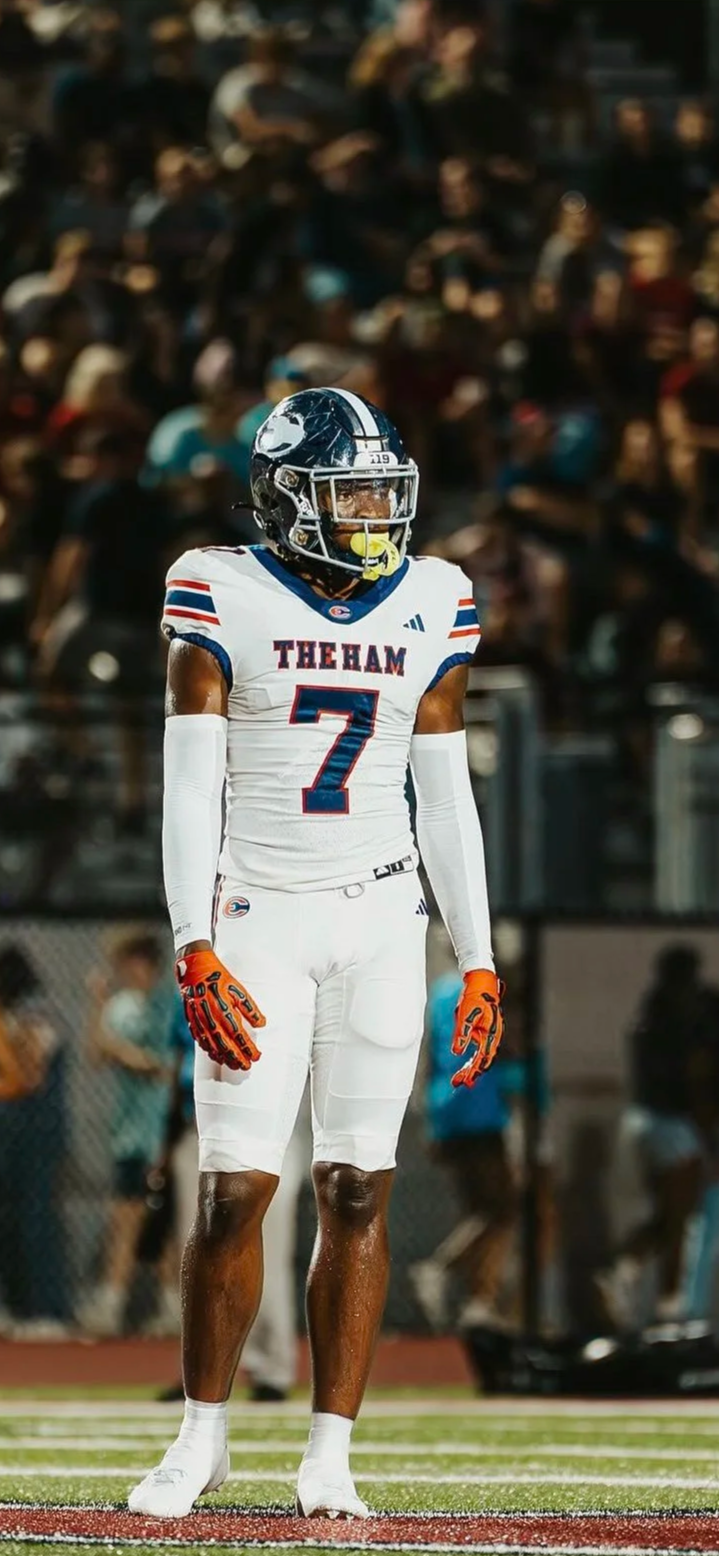 A football player standing on the field in his uniform, number 7, with a crowd in the background at a game.