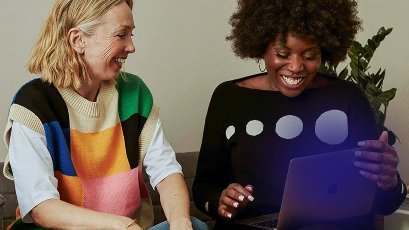 tow women sitting with a laptop smiling with a purple blurred circle overlay