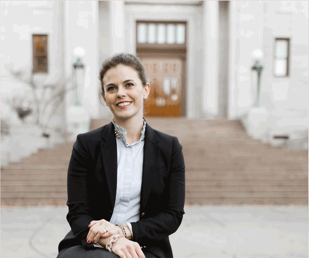 Aubree wearing a blouse and sports coat sitting in front of a building with stairs