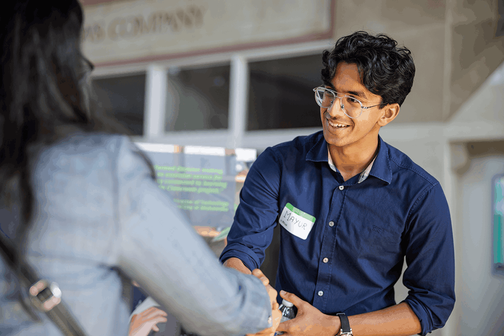 young man with glasses shaking someones hand in foreground