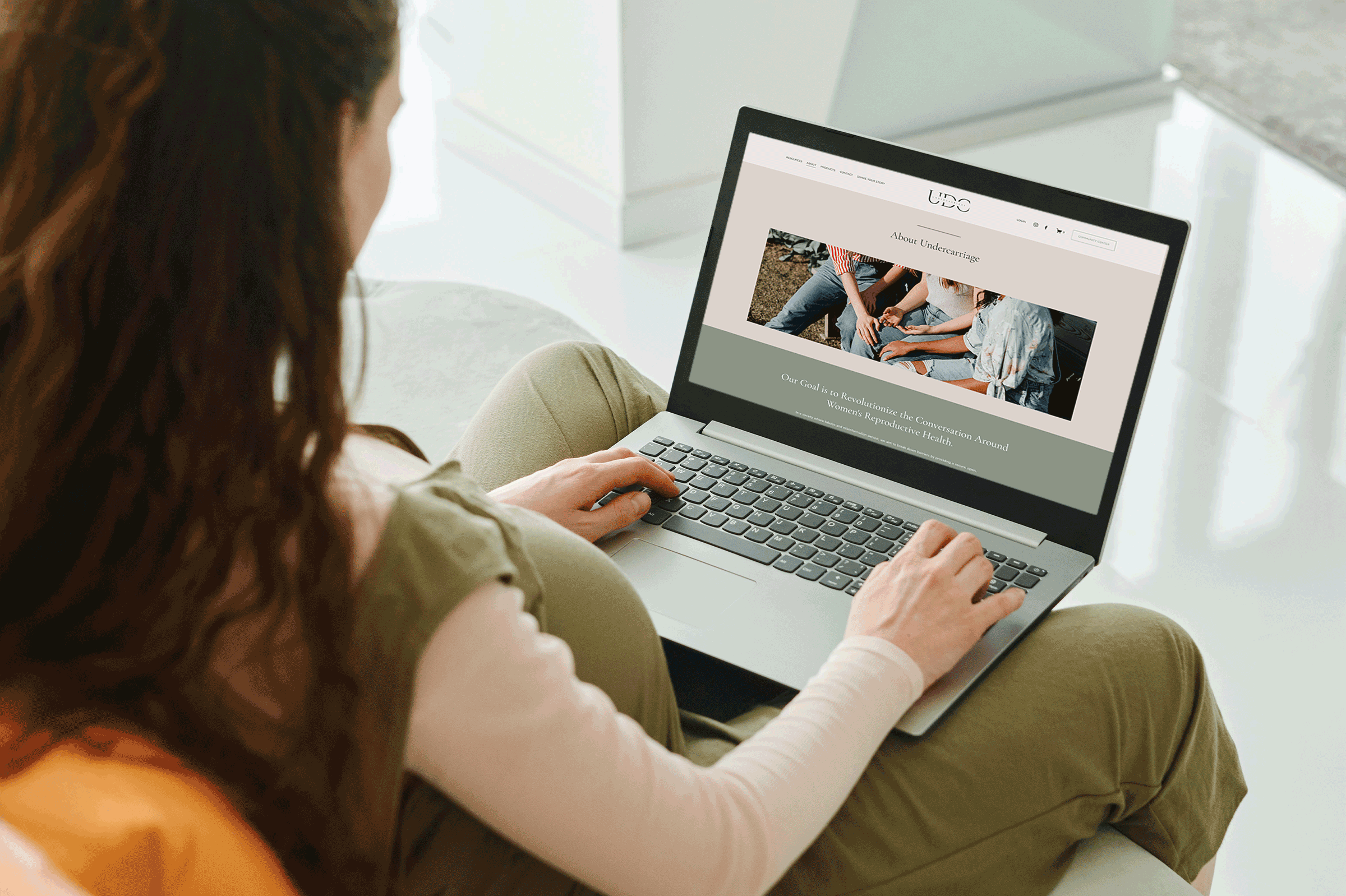 pregnant woman in a green jumpsuit looking at a laptop with a screenshot of the about page of the undercarriage website