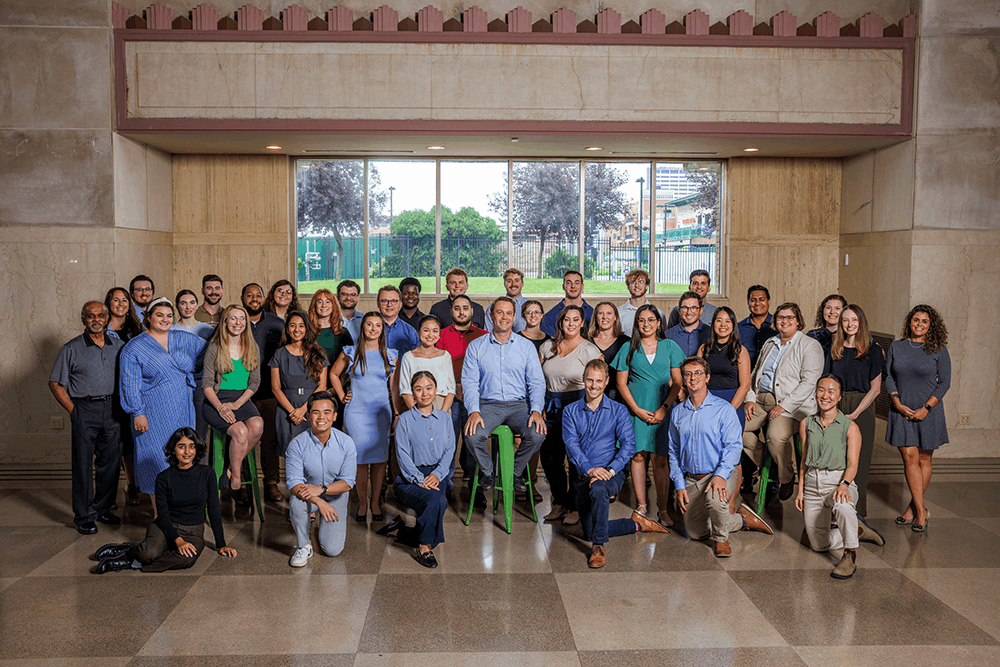 group picture of all enFocus team inside in front of a big window looking out to a park