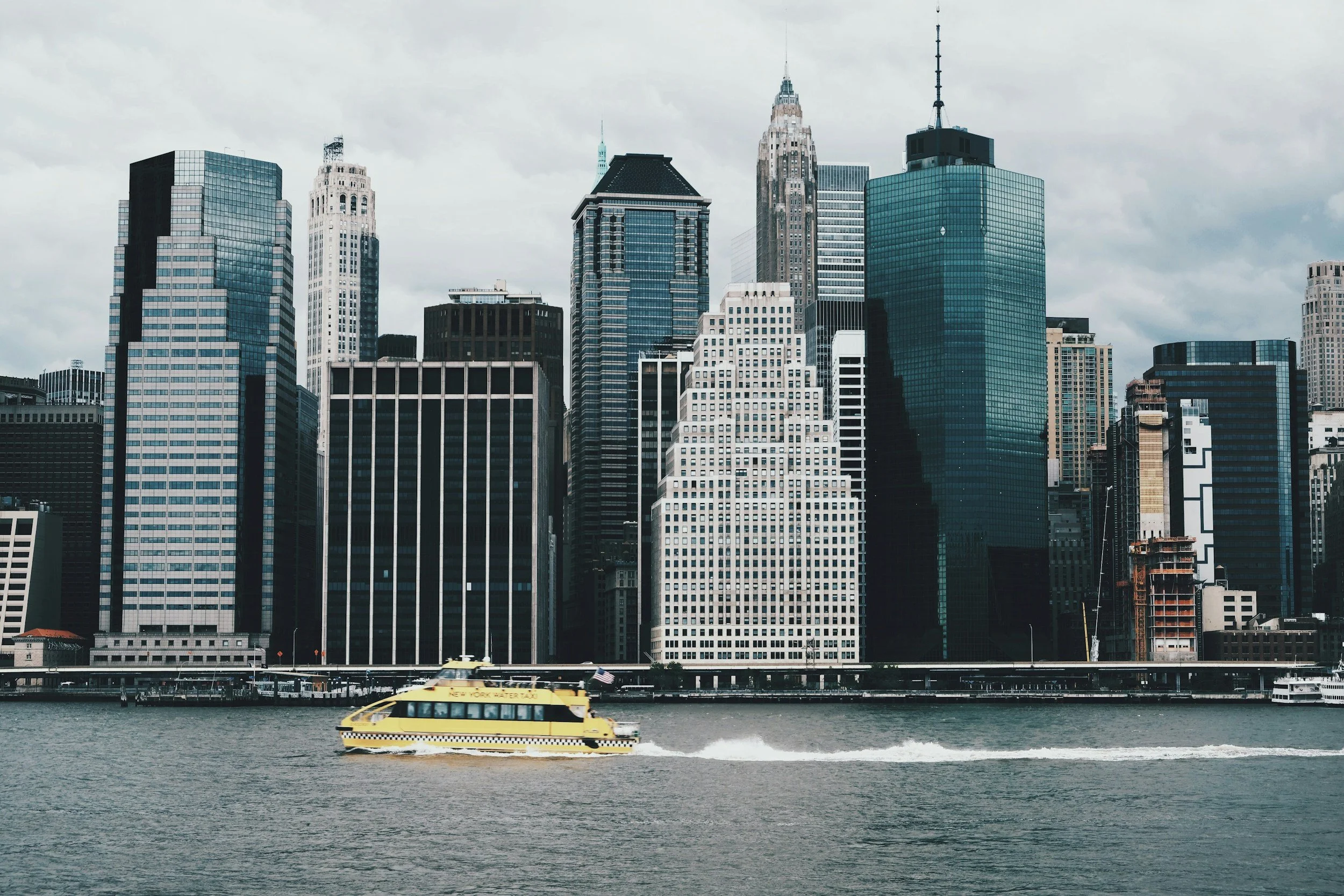 View of New York City skyscrapers with a bright yellow water taxi crossing the river in the foreground, symbolizing urban sophistication and dynamic connectivity.
