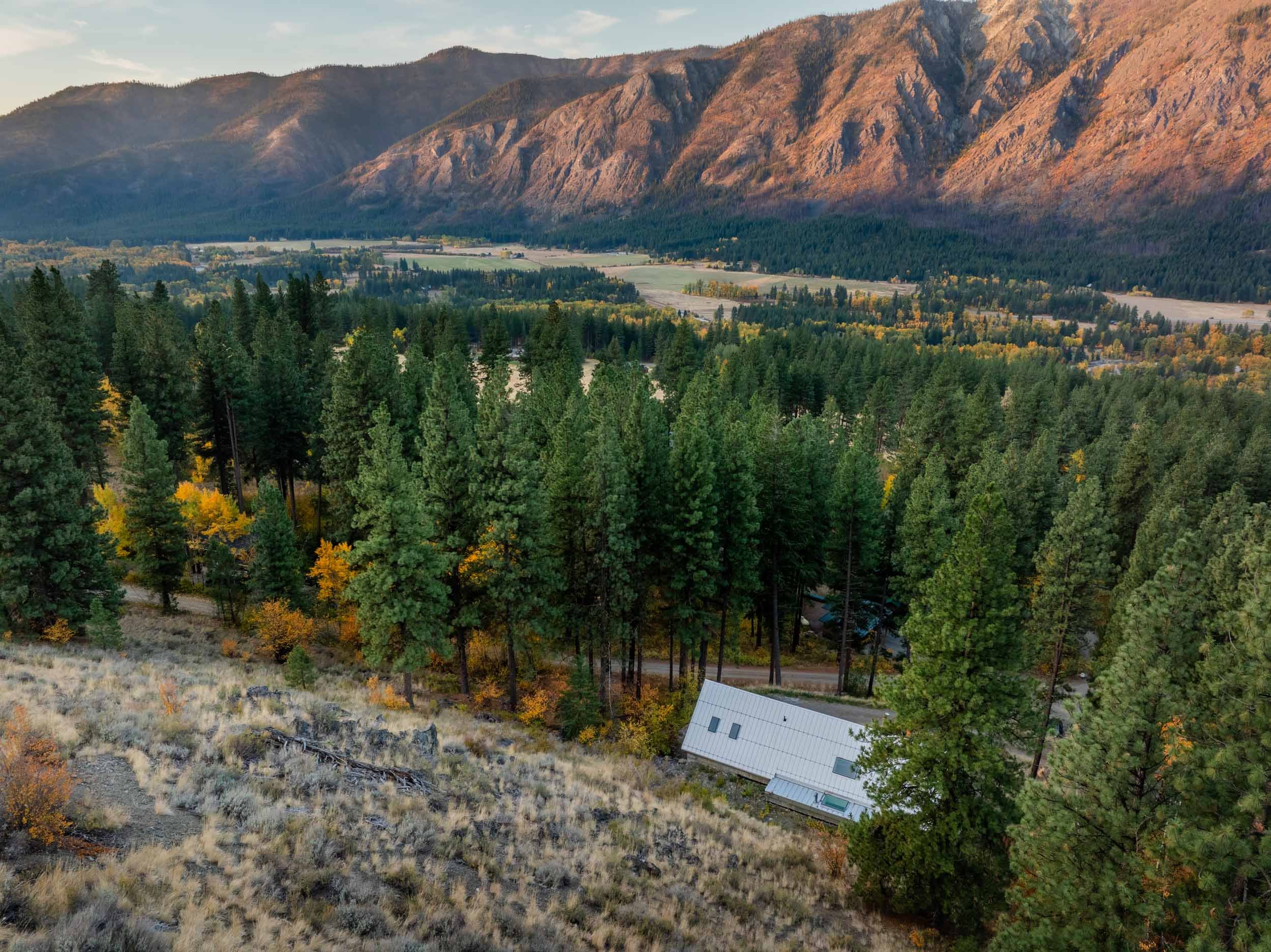 Landscape with forested hills, a small white building, and distant mountains in autumn colors.
