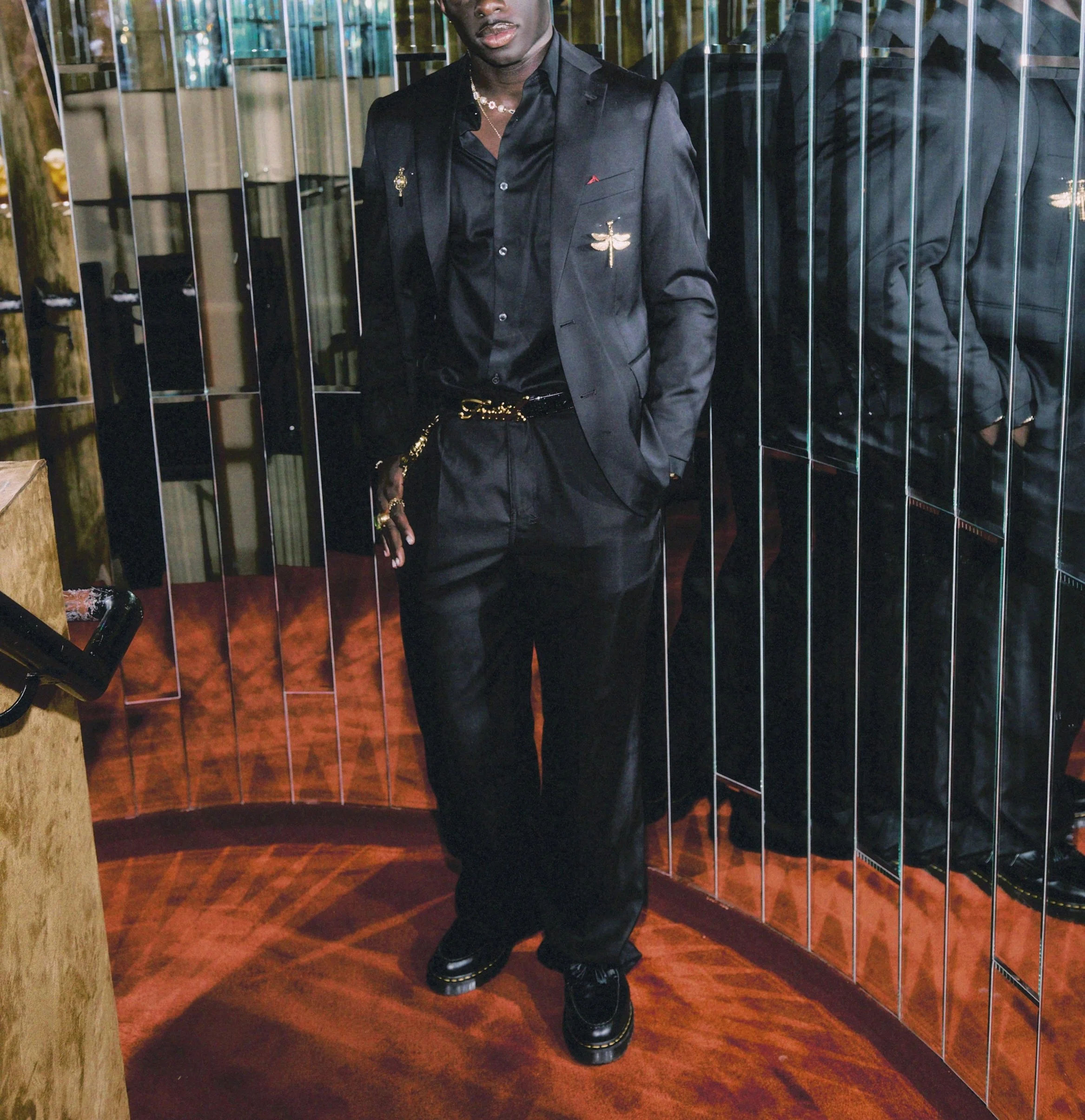 Man in a black satin suit posing in mirrored walls at a stylish cocktail lounge in Soho New York City