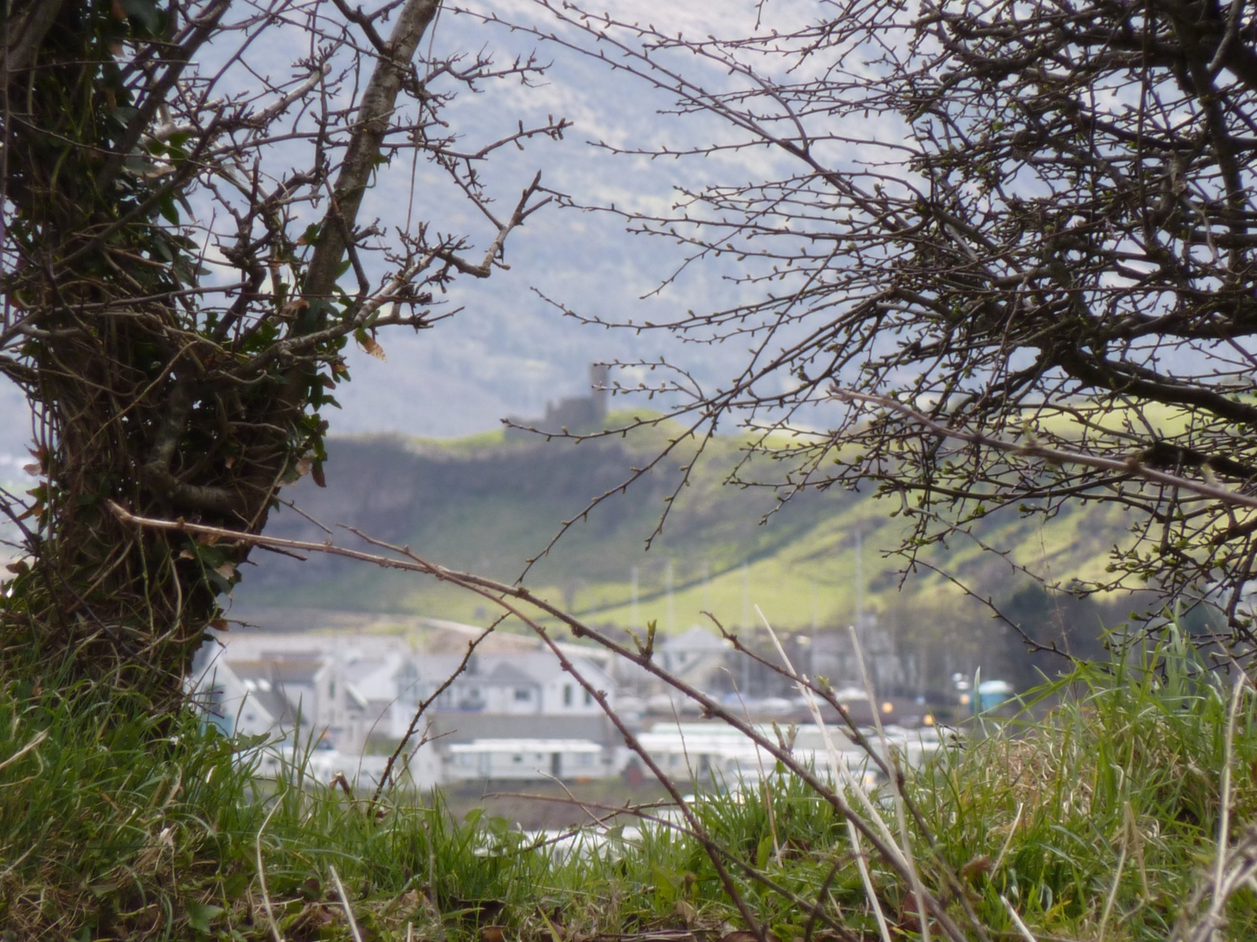 Scenic view of a small building on a grassy hill with a backdrop of snow-capped mountains.