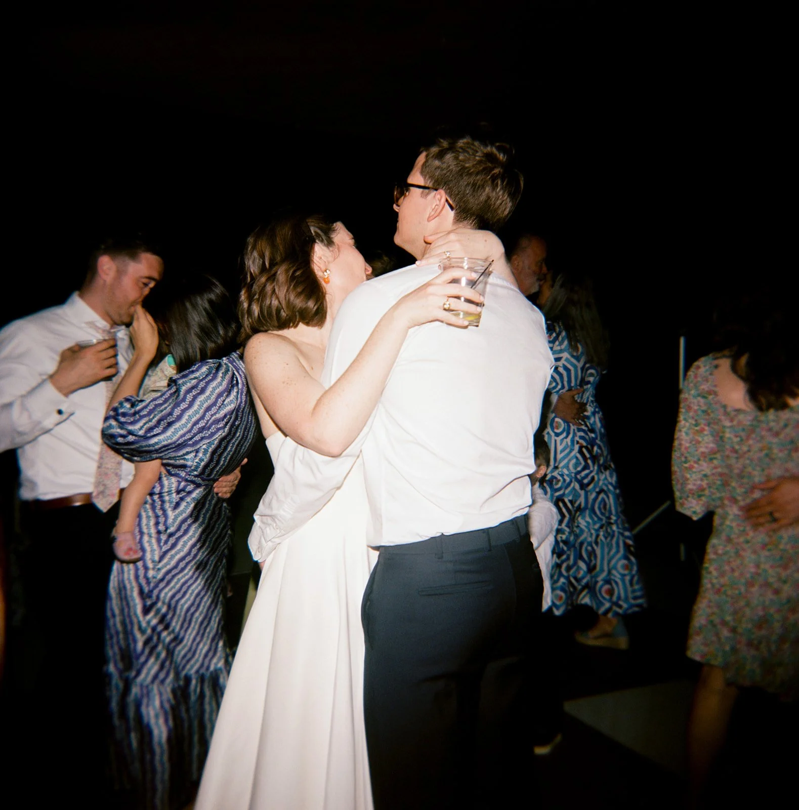 A bride and groom share a dance at their wedding reception, surrounded by guests.