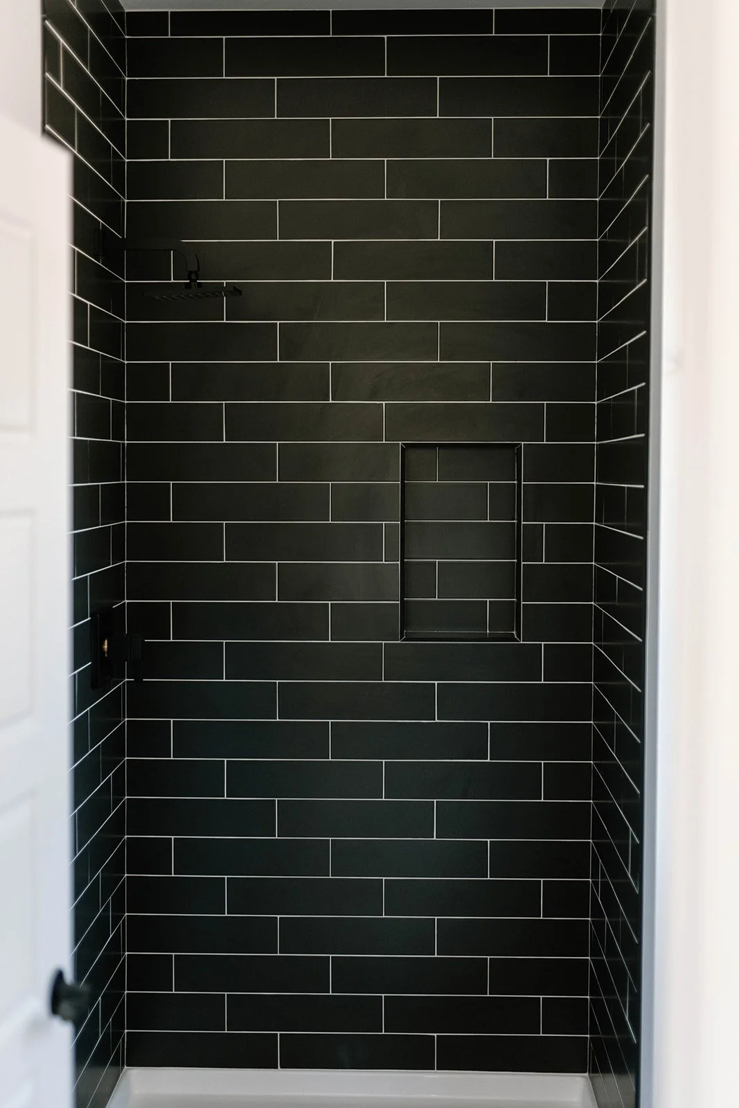 Black subway tile shower with niche.