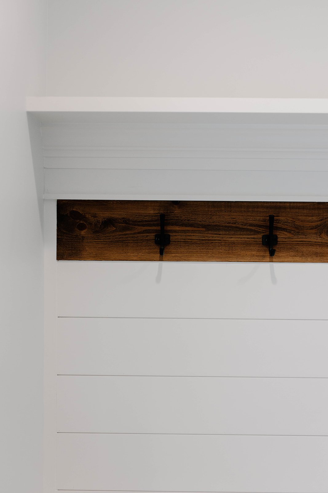 Custom built lockers with cubbies and a stained detail below the shelf with black hooks.