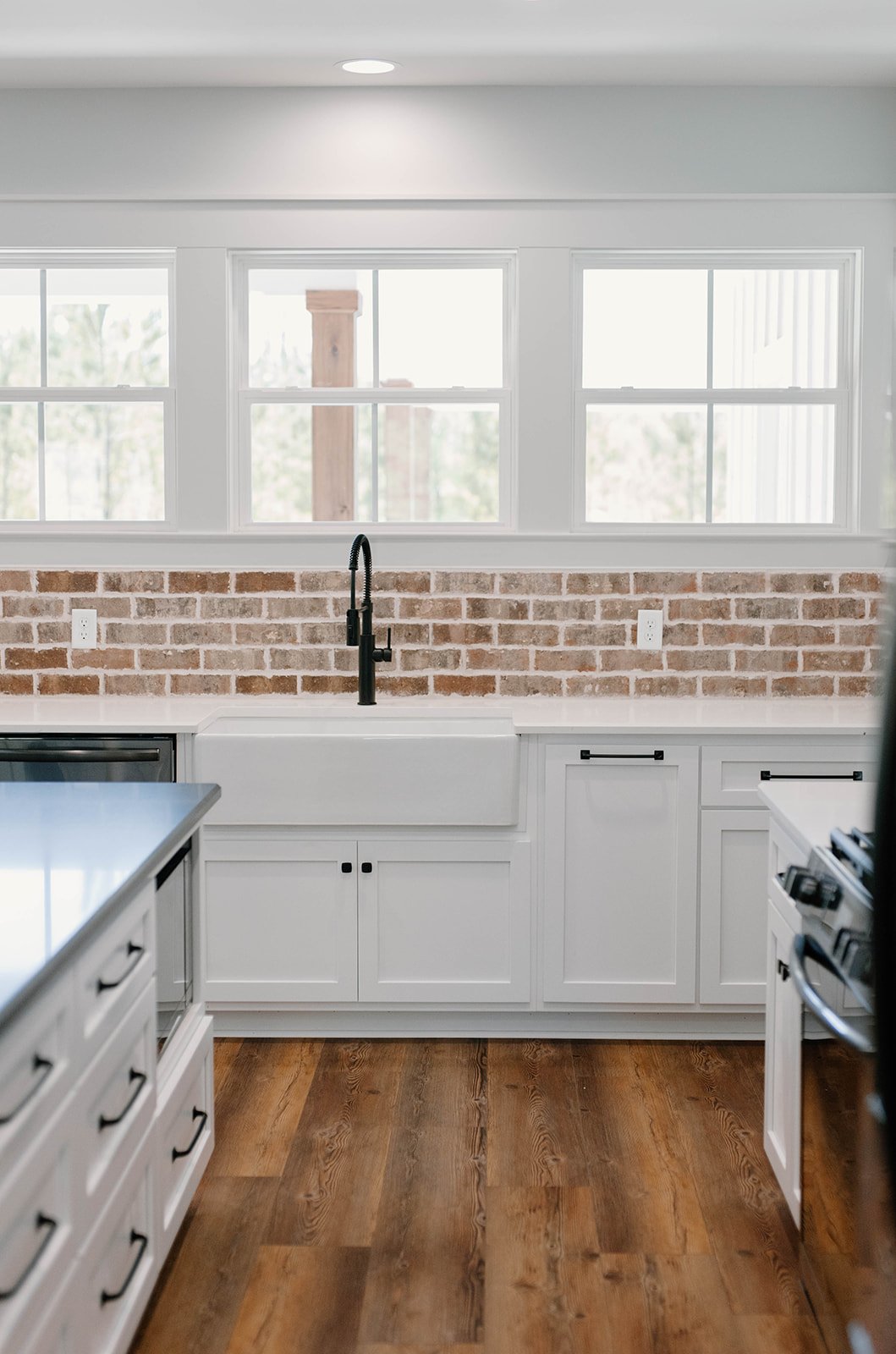 Custom kitchen cabinets in white with a brick backsplash and matte black hardware and fixtures and a farmhouse sink.