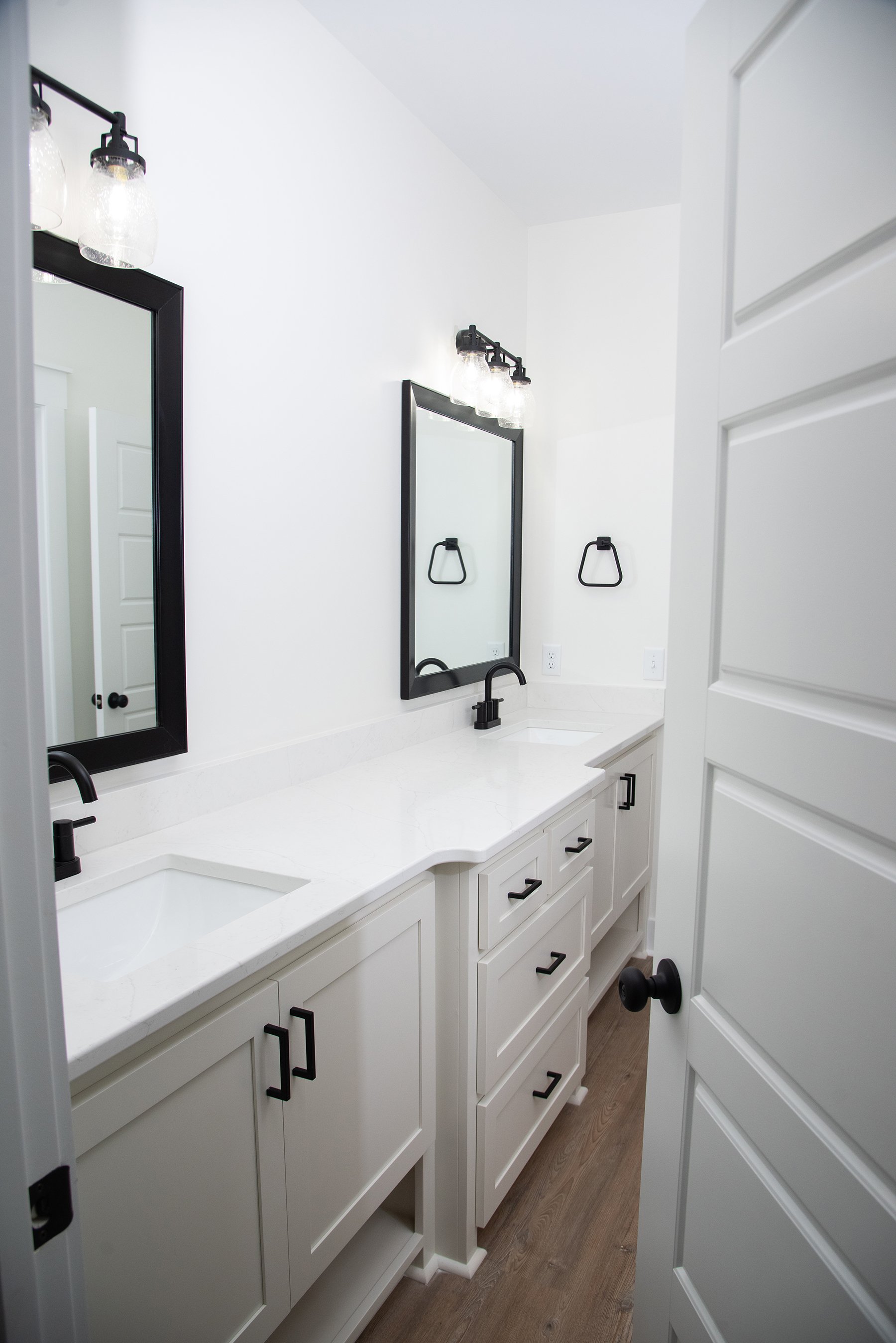 Jack and Jill bathroom with custom built vanity cabinets with black hardware. Includes black finish vanity lights and black trimmed mirrors.