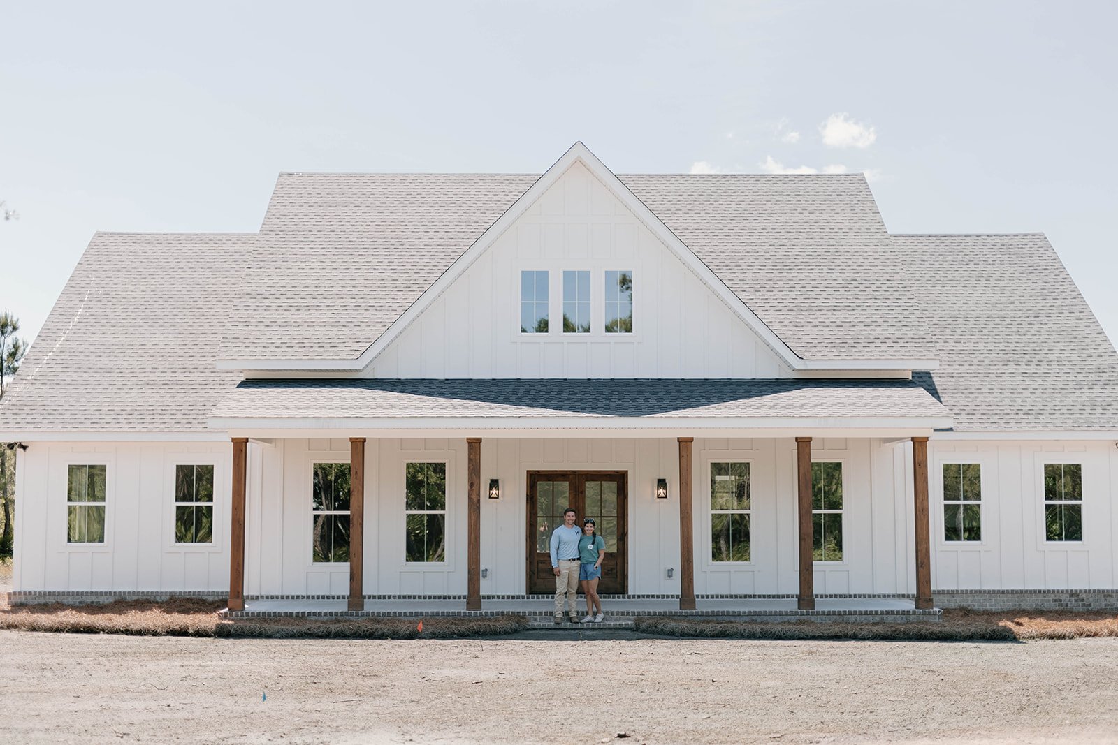 Home builder couple standing in front of a modern white farmhouse.