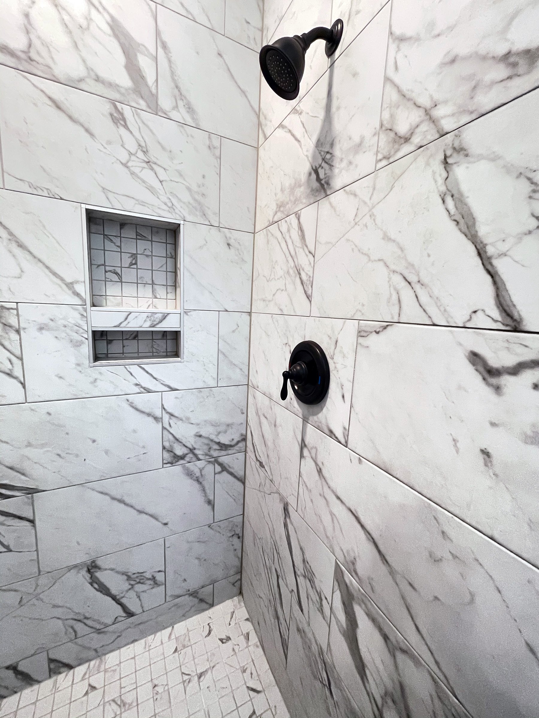 Master bathroom walk in shower with glass door and black shower head and valve and a niche.