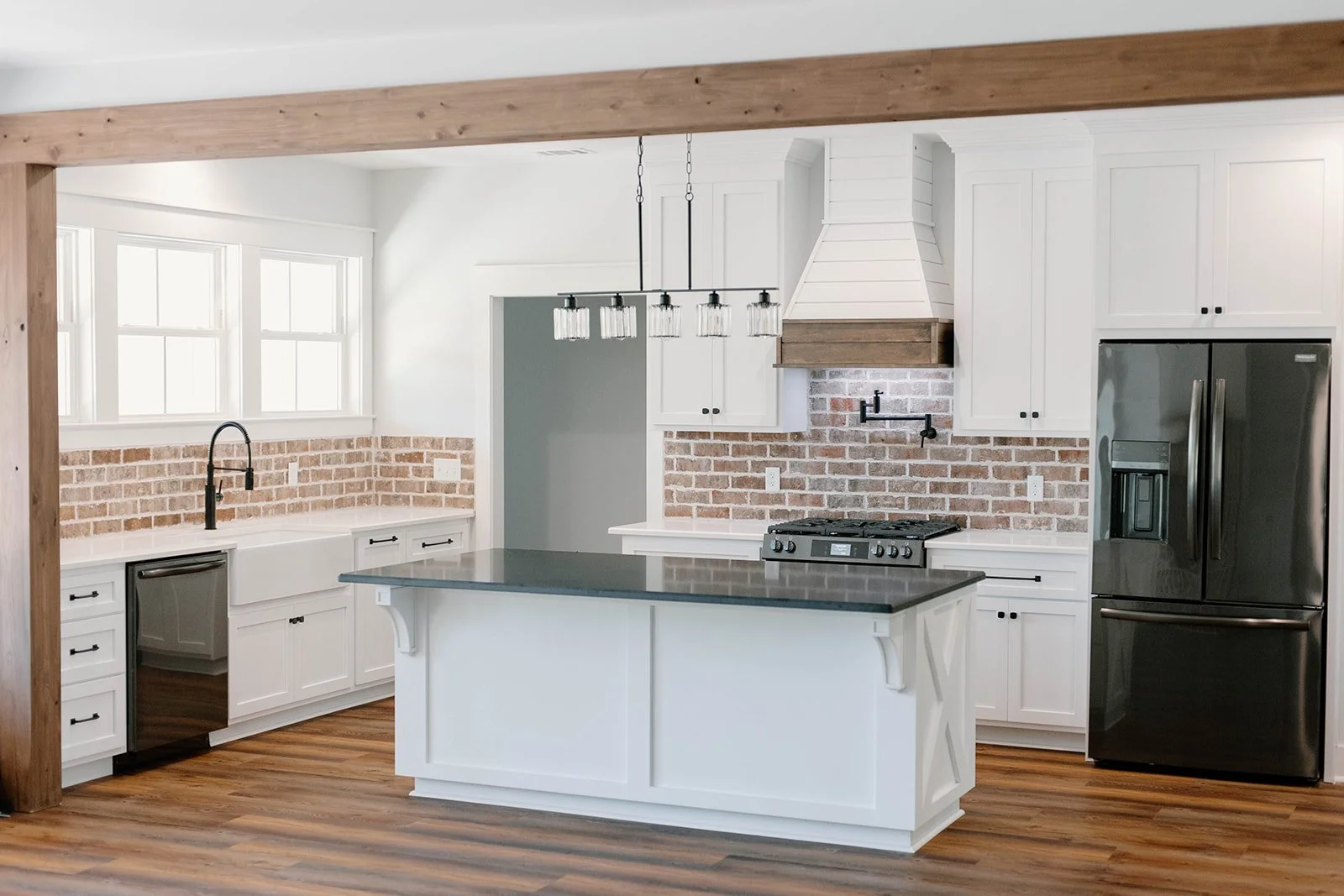 complete farmhouse kitchen with brick backsplash, shiplap range hood, white cabinets, black countertops and cypress cased opening