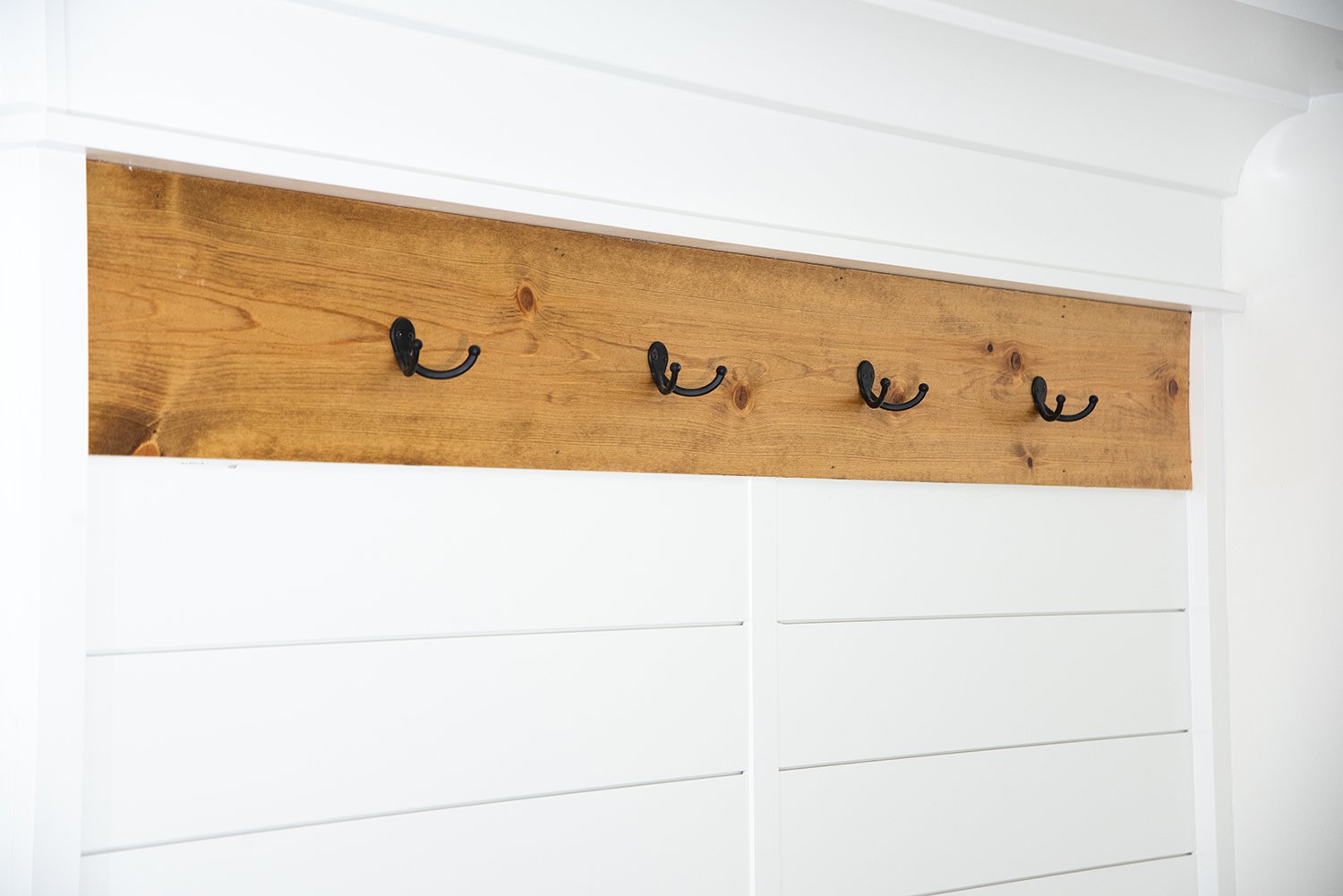 Custom built locker with black hooks on a stained wood accent.