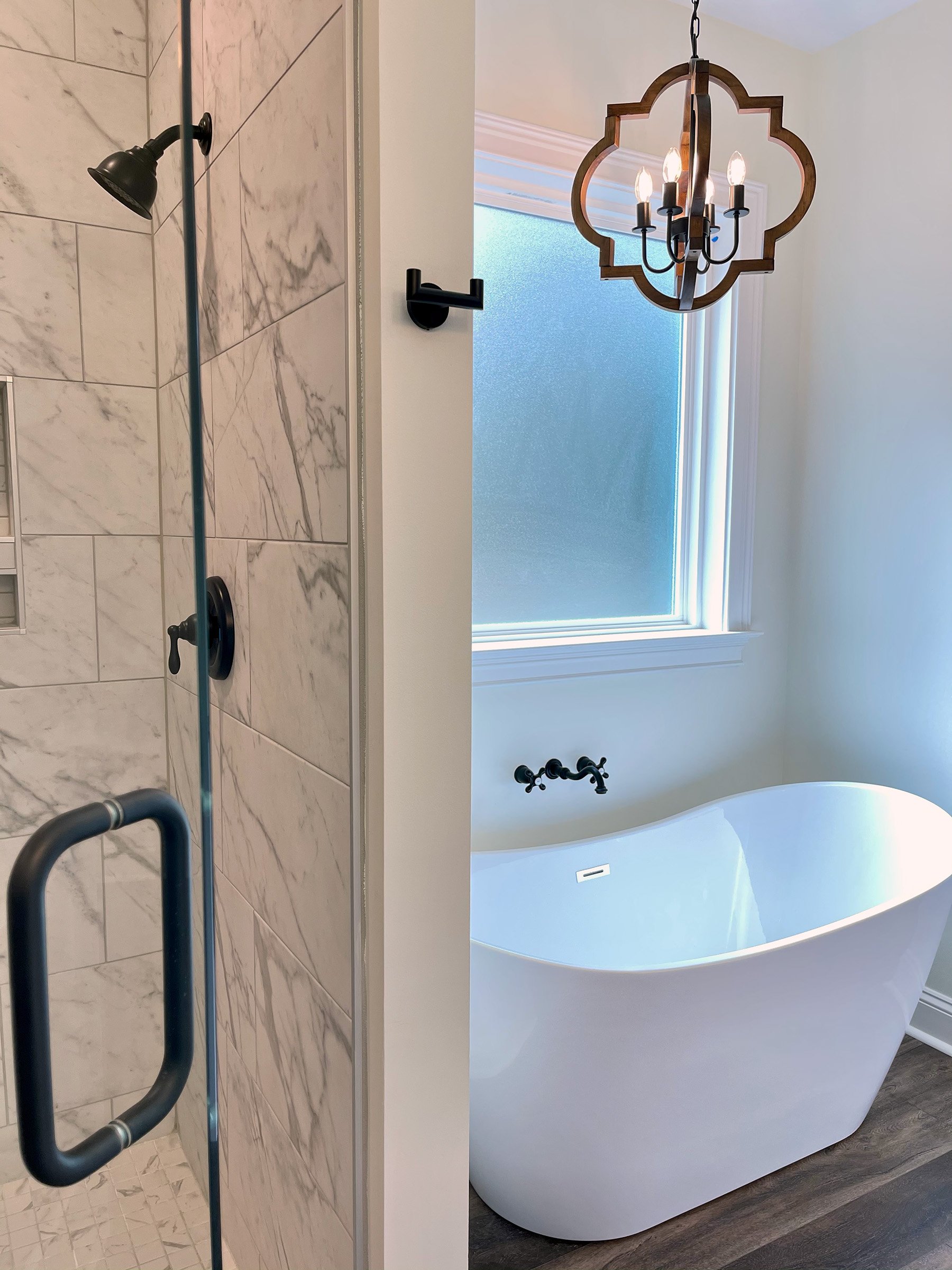 Master bathroom with custom tile shower with glass door and freestanding tub with wood and black finish chandelier and wall mounted tub filler.