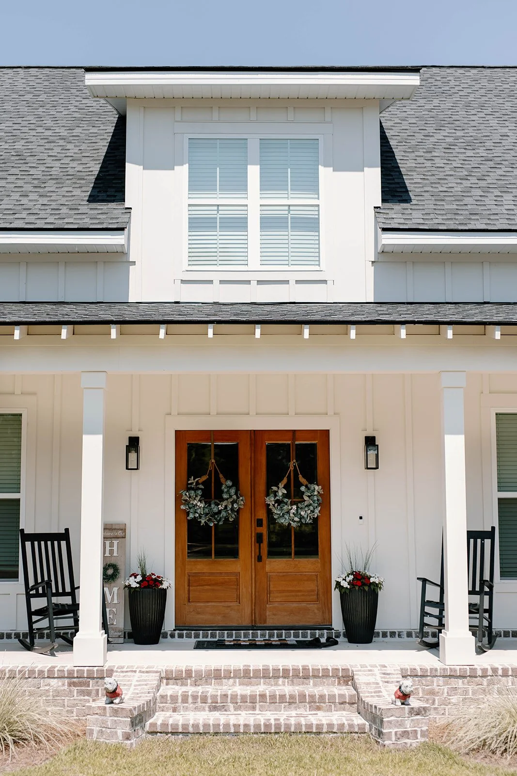 A low-country style modern farmhouse that includes board and batten Hardie siding in Oyster White by Sherwin Williams and includes a single shed dormer, rafter tails and a custom wood stained door in Golden Oak by Minwax.