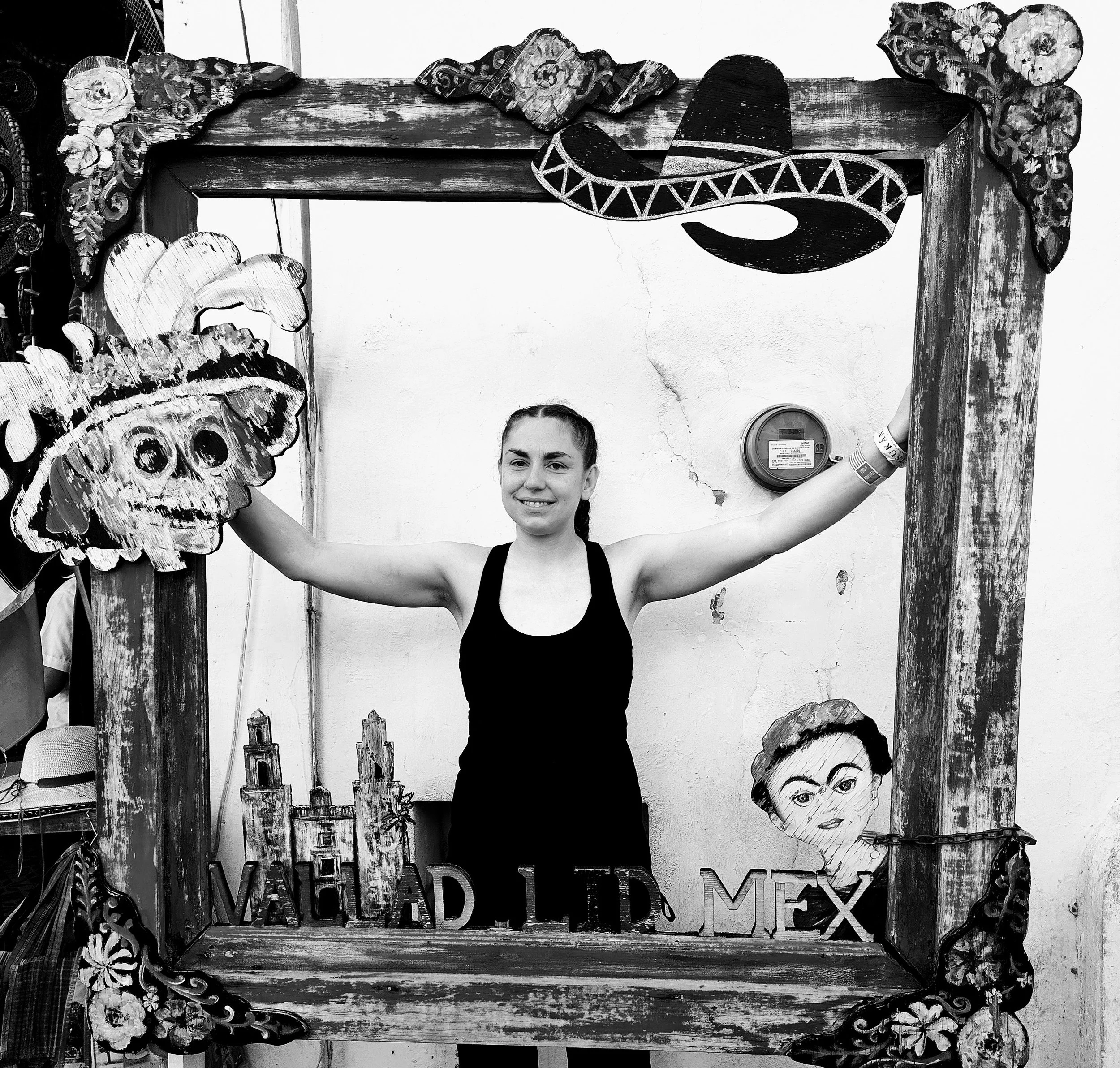 Black and white photo of a carved wooden frame with a outset archway, floral patterns, and a painted Mexican mask on the right side.