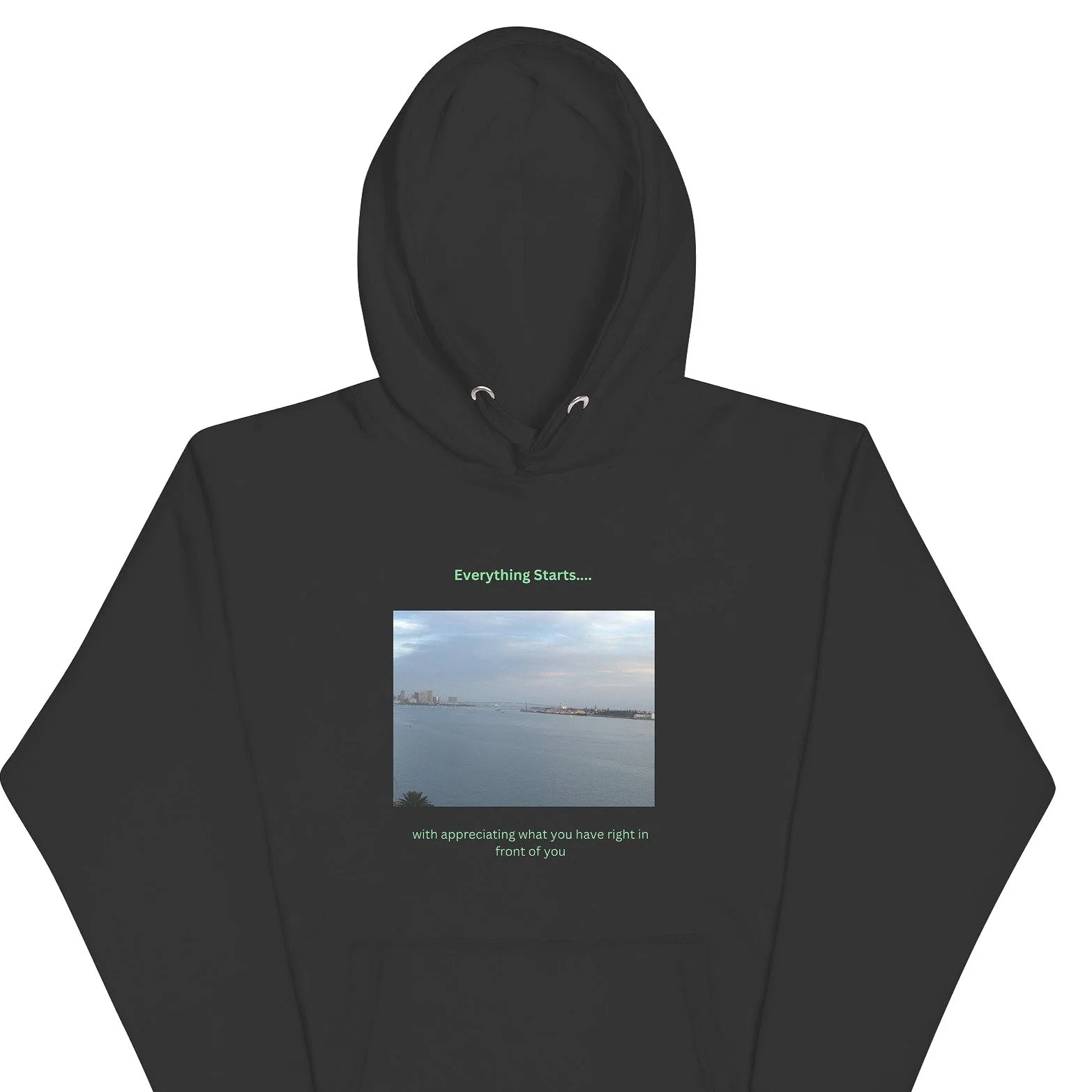 Black hoodie with a landscape photo of a river, cityscape, and sky on the front, and the text 'Everything Starts... with appreciating what you have right in front of you' in green.