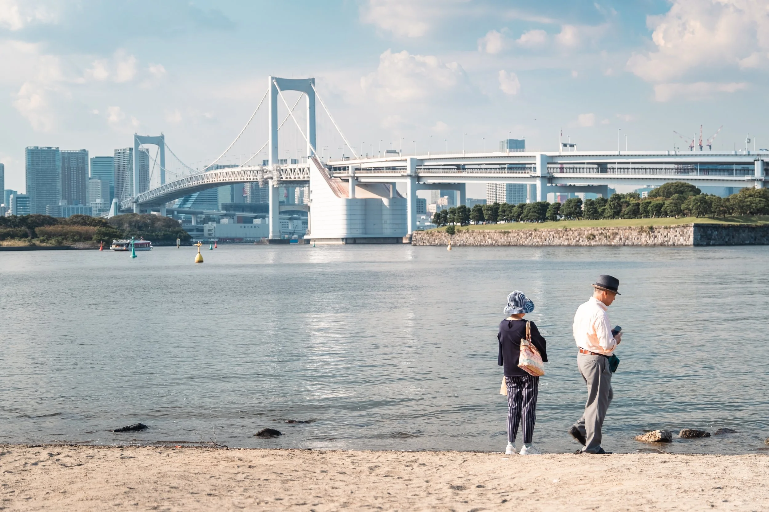 An elderly couple taking in the views of the Rainbow Bridge, at Odaiba Beach