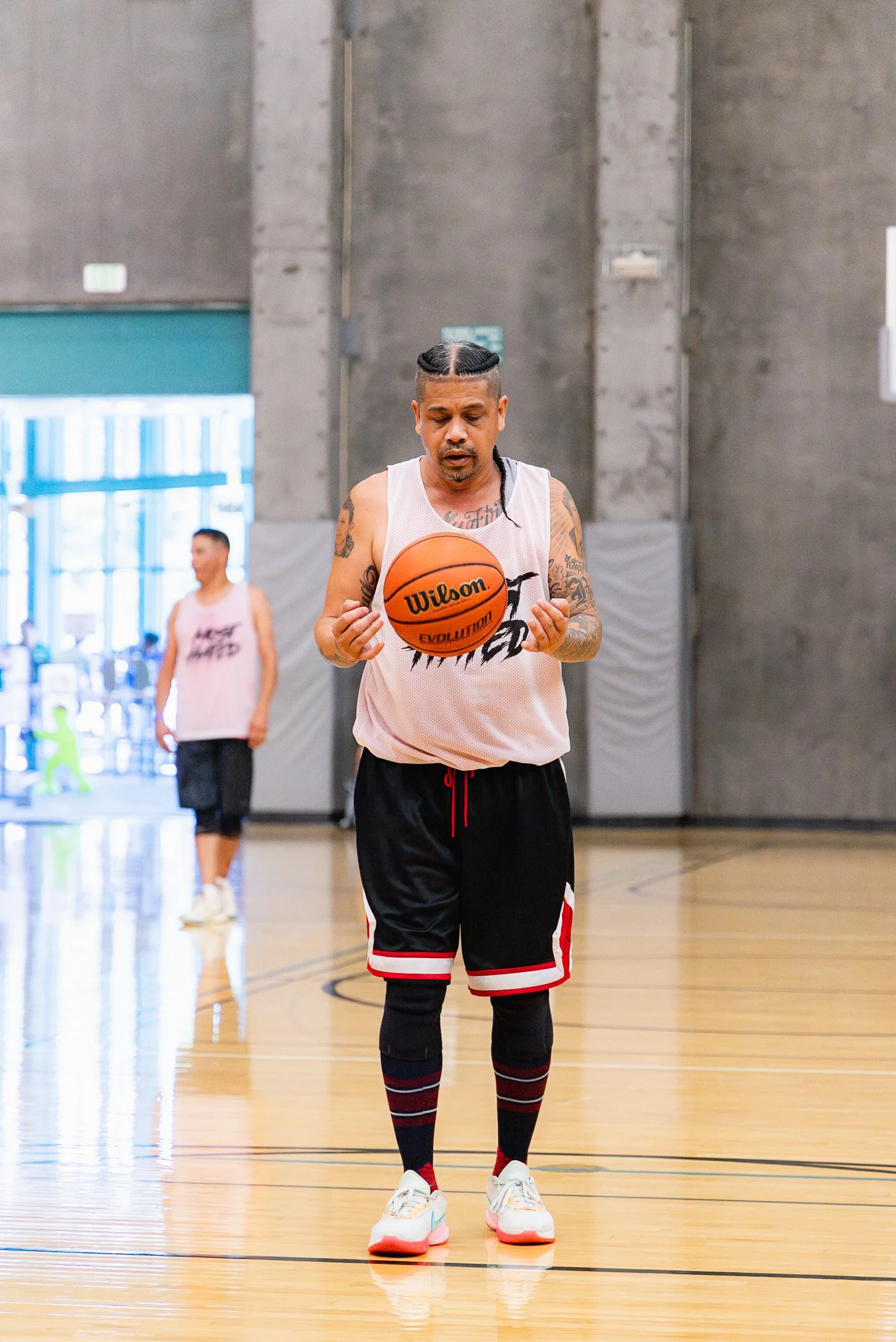 A man holding a basketball on a gym court with another man in the background.