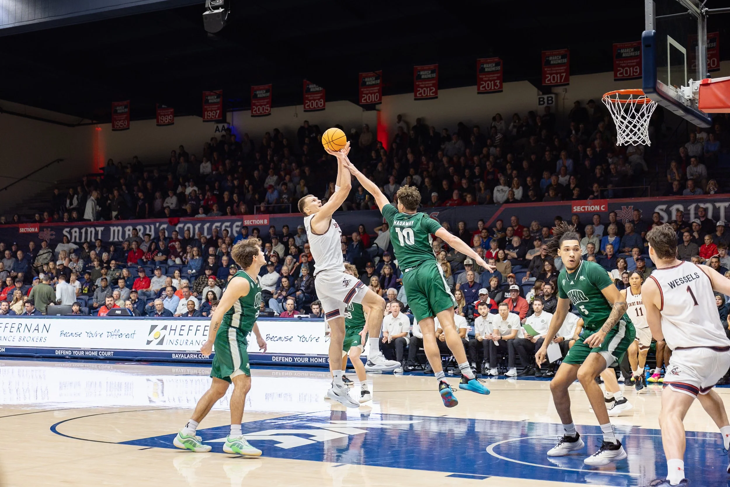 Basketball game with players from two teams competing near the hoop during a game at Saint Mary’s College, with an audience watching in the background.