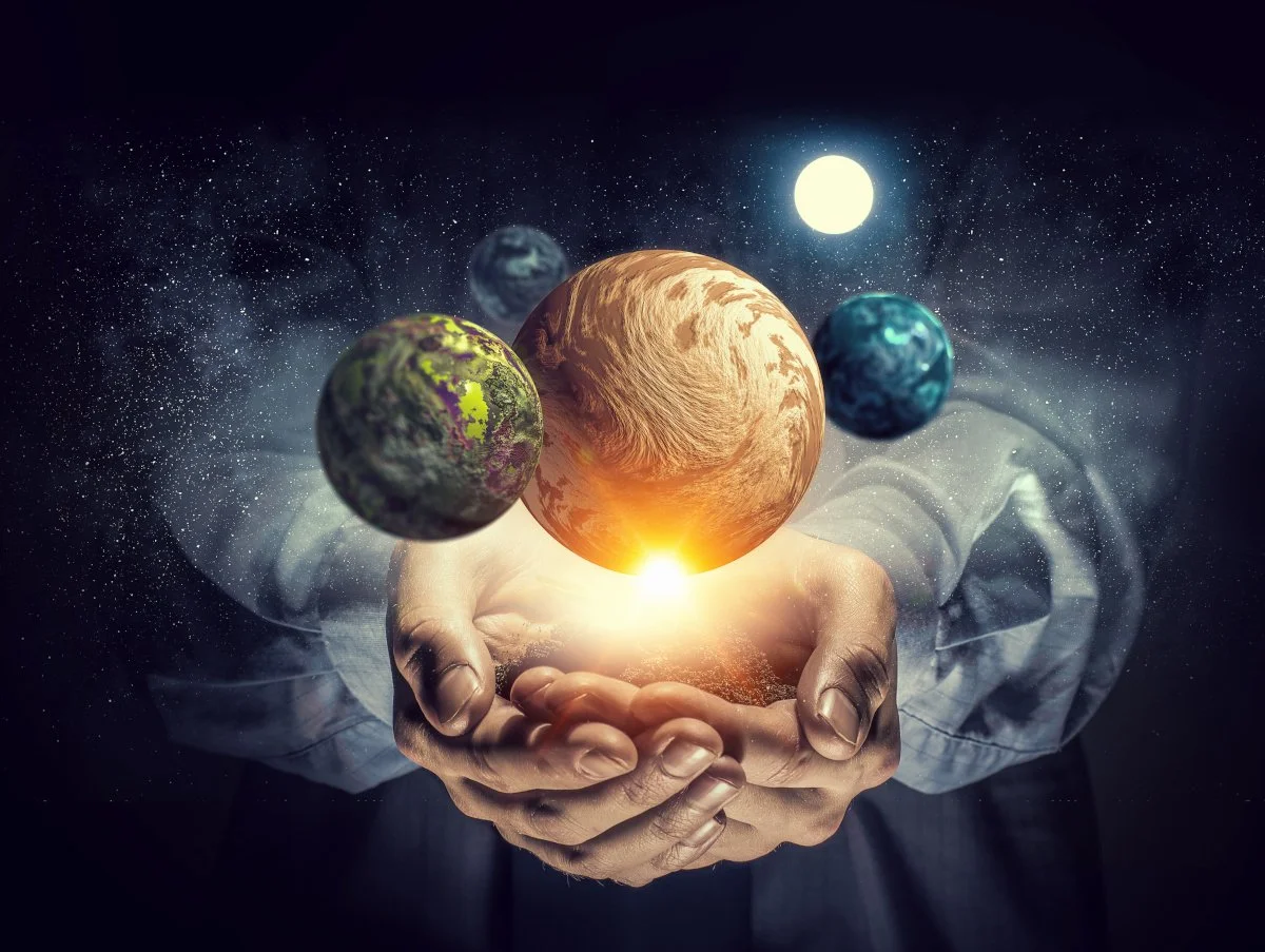 Hands holding miniature planets in space with a glowing sun, starry background, and a person in a suit.