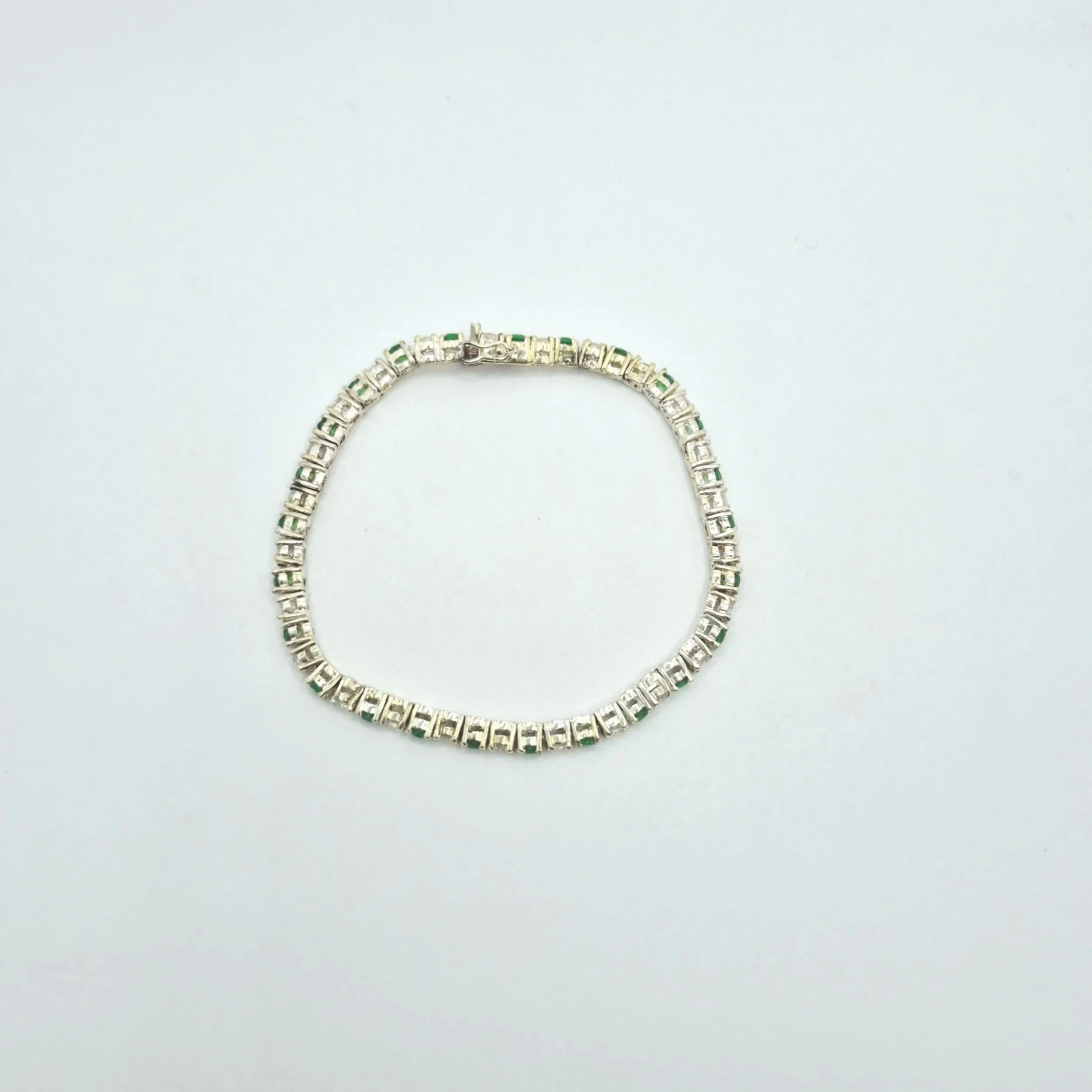 Close-up of emerald-style silver bracelet with alternating green and white gems