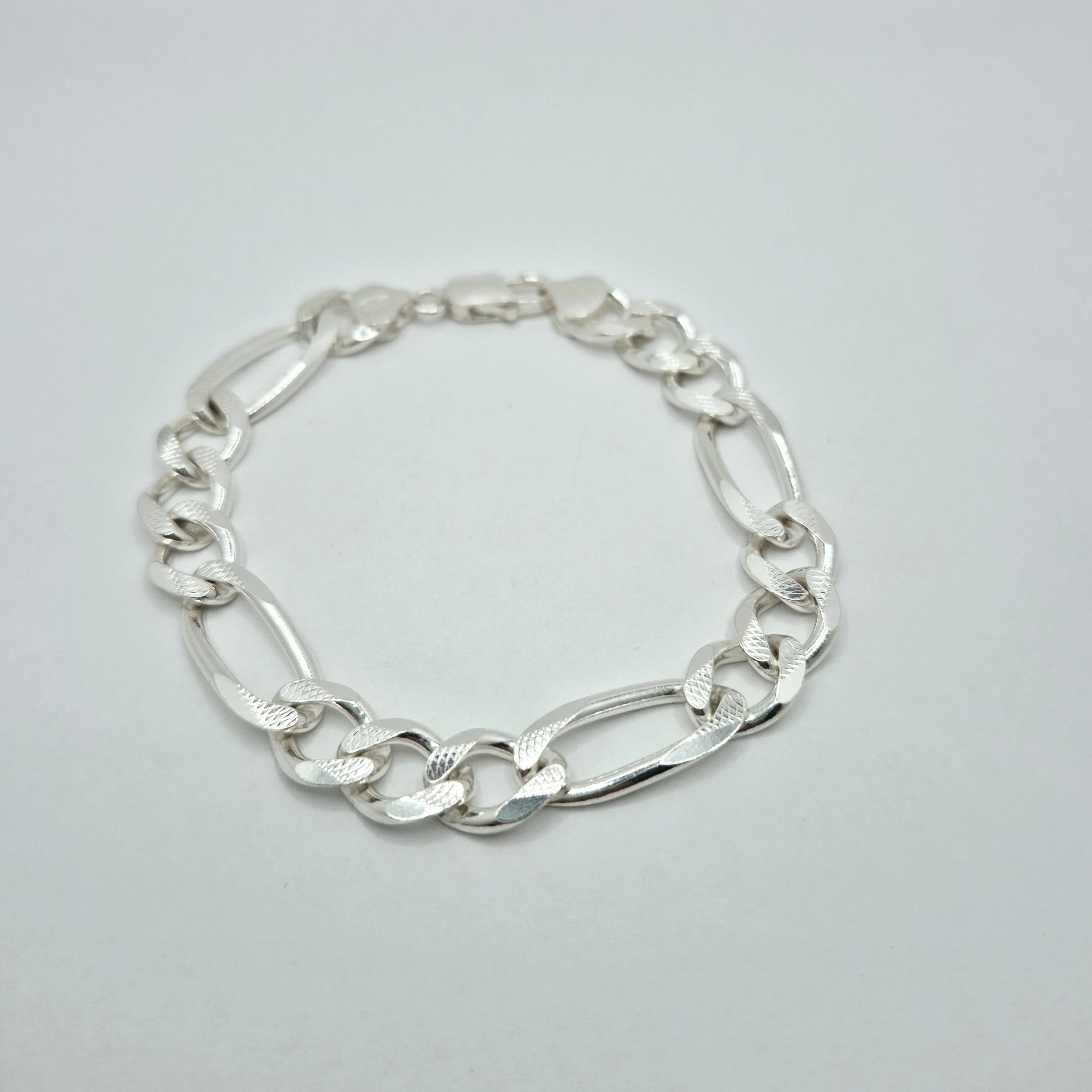 Bold silver bracelet with thick textured links laid flat on white background