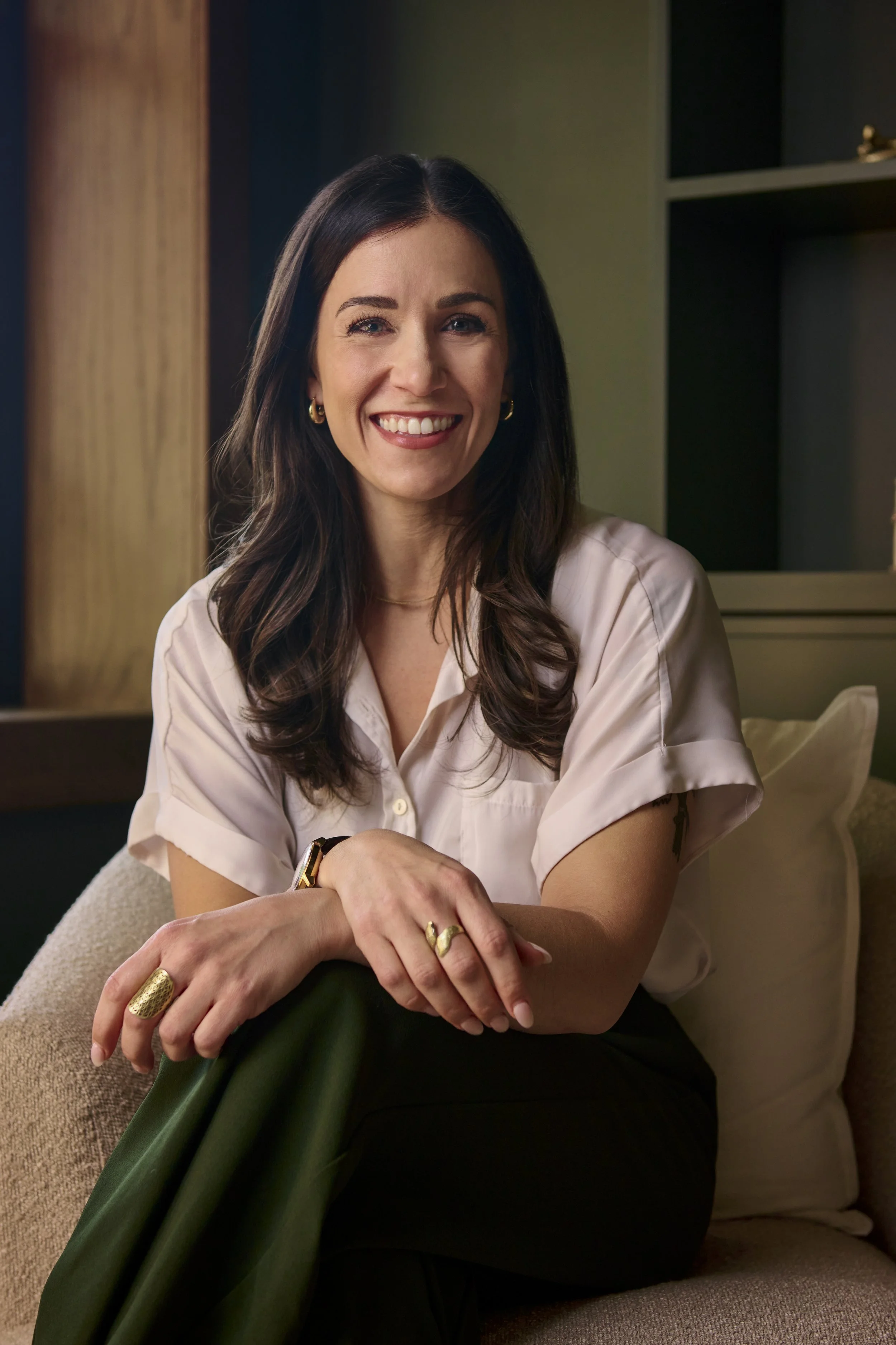 Valerie Mirza sitting on a tan chair with arms crossed over lap