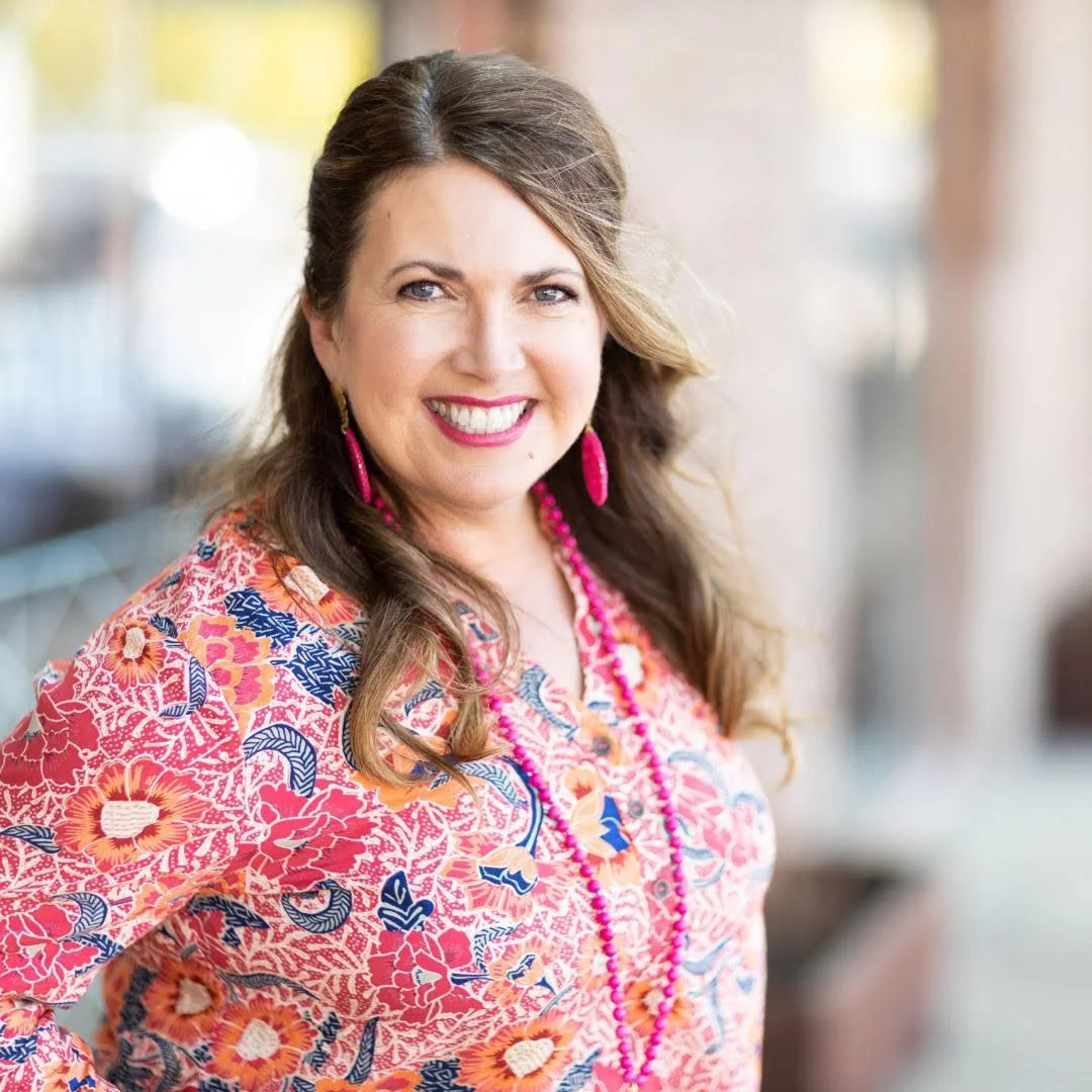 Marilyn Dollar smiling outside in a floral shirt with pink earrings and a necklace.
