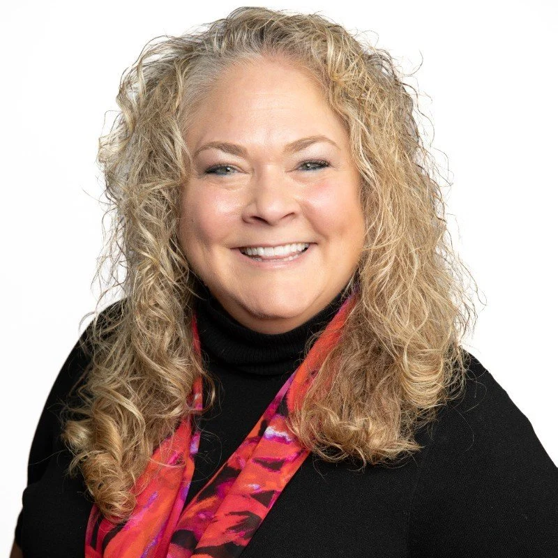 Heather Bailey smiling in black top and floral scarf
