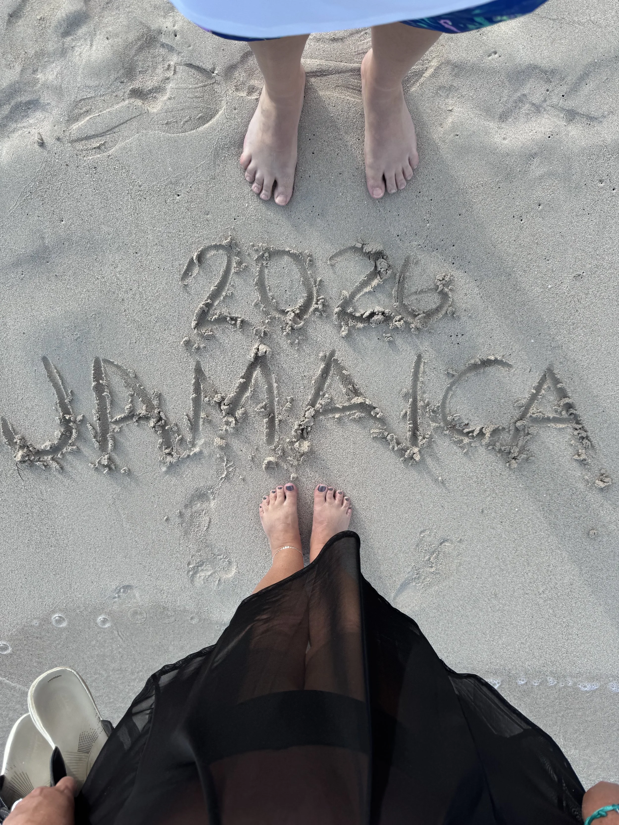 2026 Jamaica” written in the sand with our feet on the beach