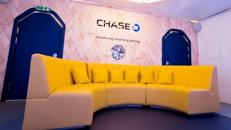 Chase Bank display with yellow curved sofa and promotional sign reading ‘Introducing rewarding banking’ inside a modern lounge area.