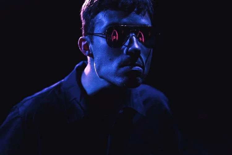 Actor performing in There Is a War at IAB, captured in dramatic blue lighting with reflective sunglasses.