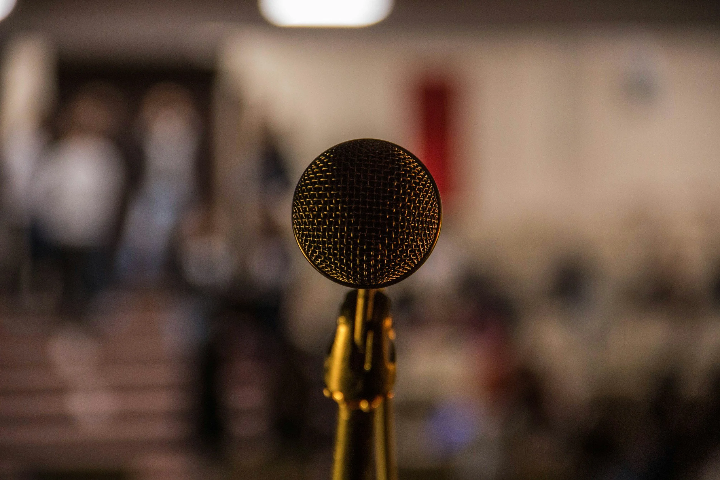 Close-up of a microphone on a stand, focused, with a blurred background.
