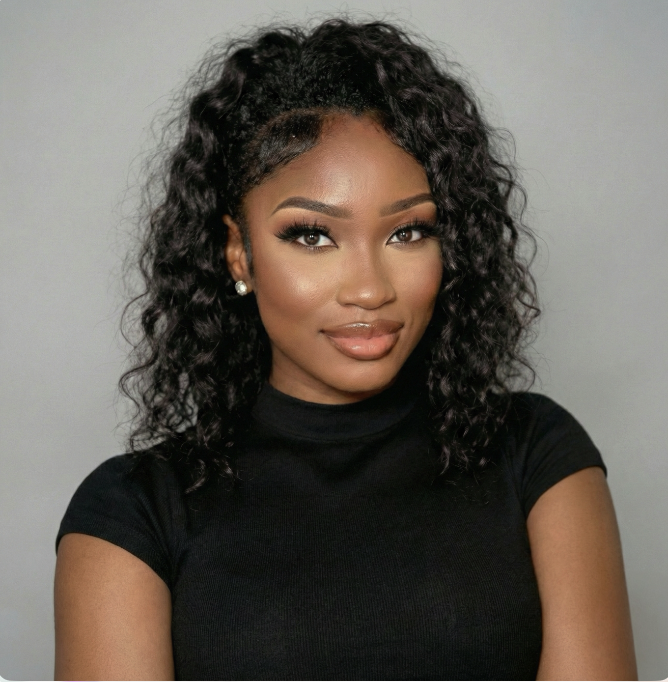Portrait of a woman with dark curly hair, wearing a black top and pearl earrings, smiling softly against a neutral background.