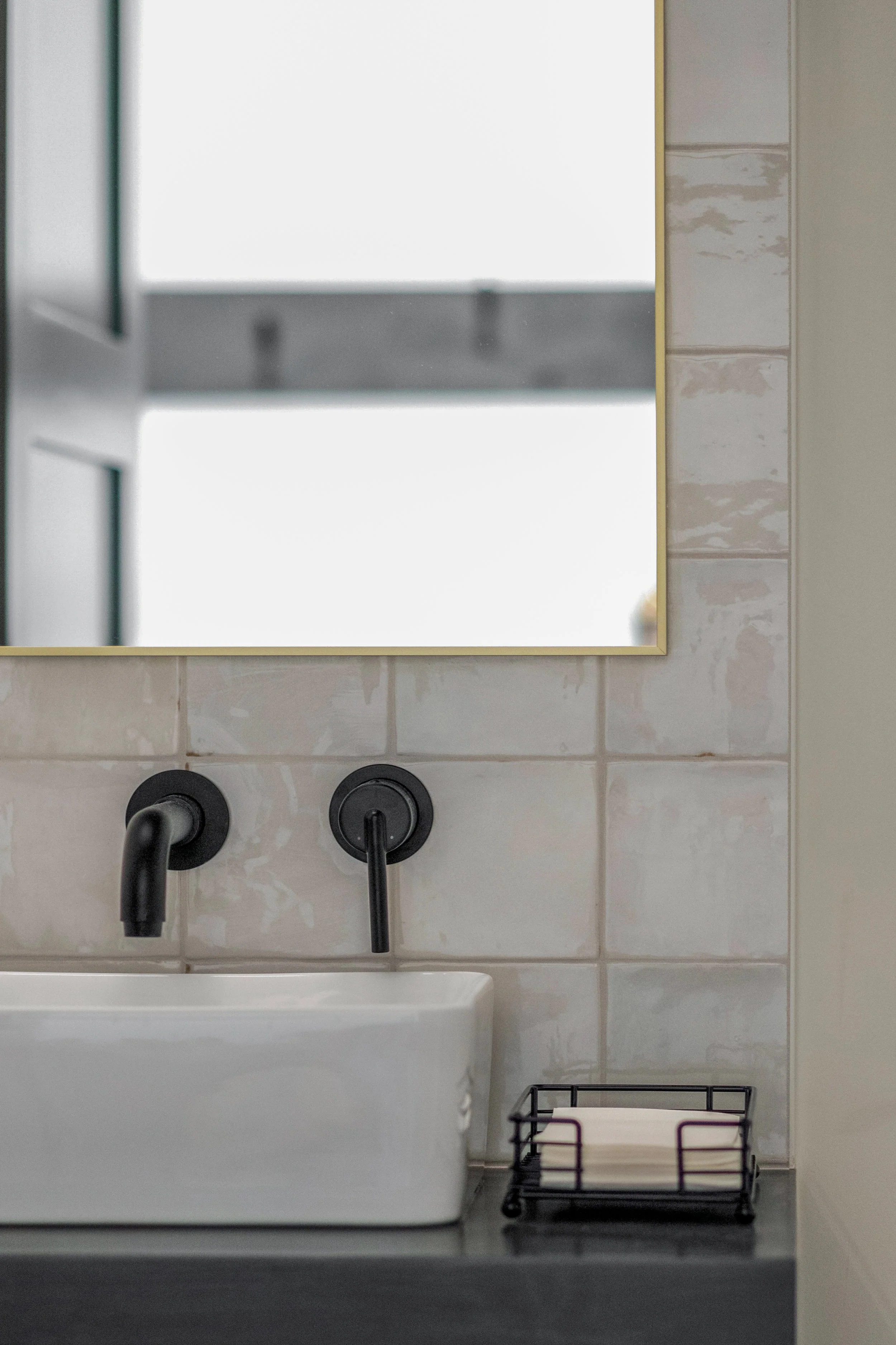 Bathroom sink with black faucet and handle, mirror above, small black rack with folded white towels, beige tiled wall.