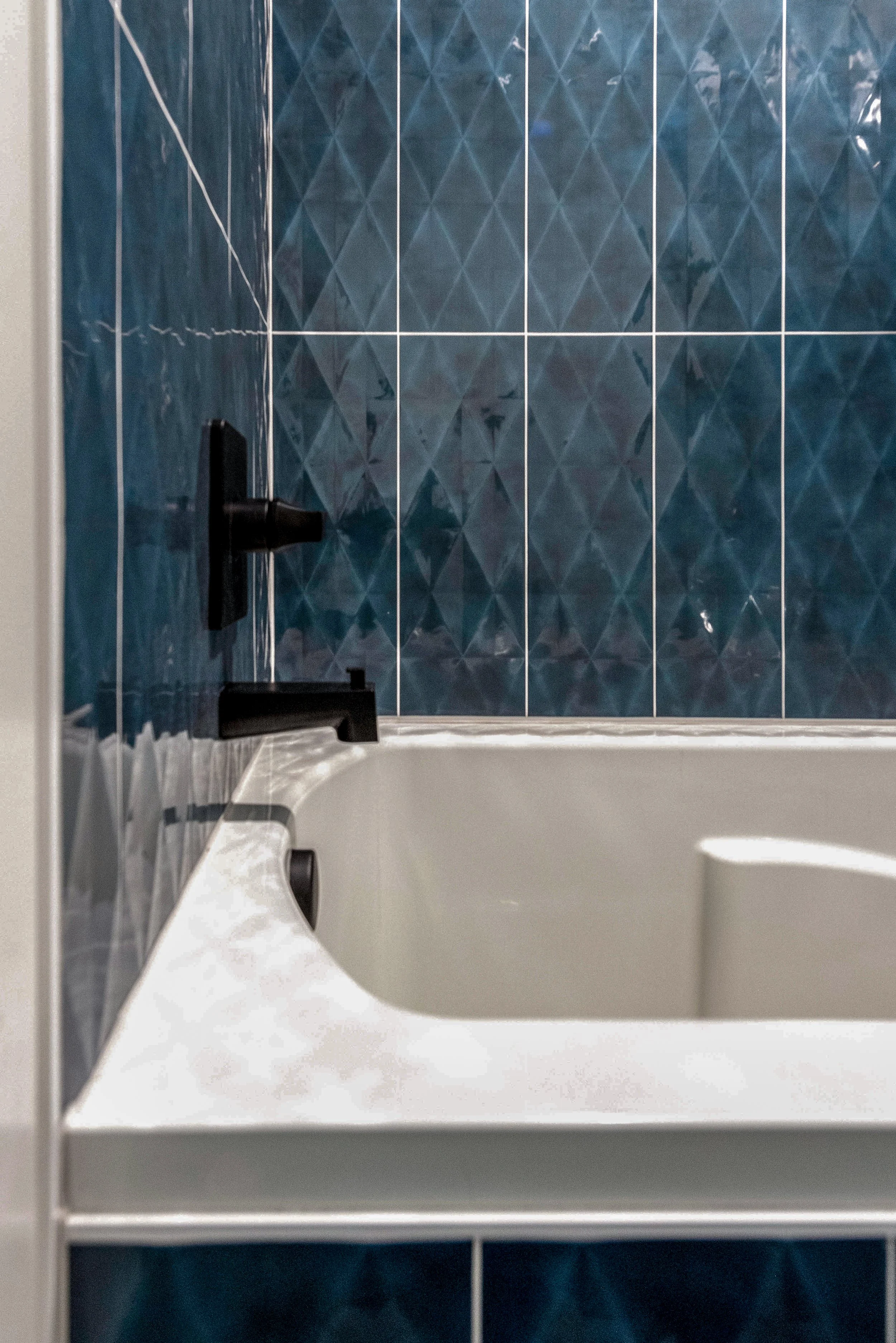 Close-up of a white bathtub with a black faucet against a blue tiled wall.