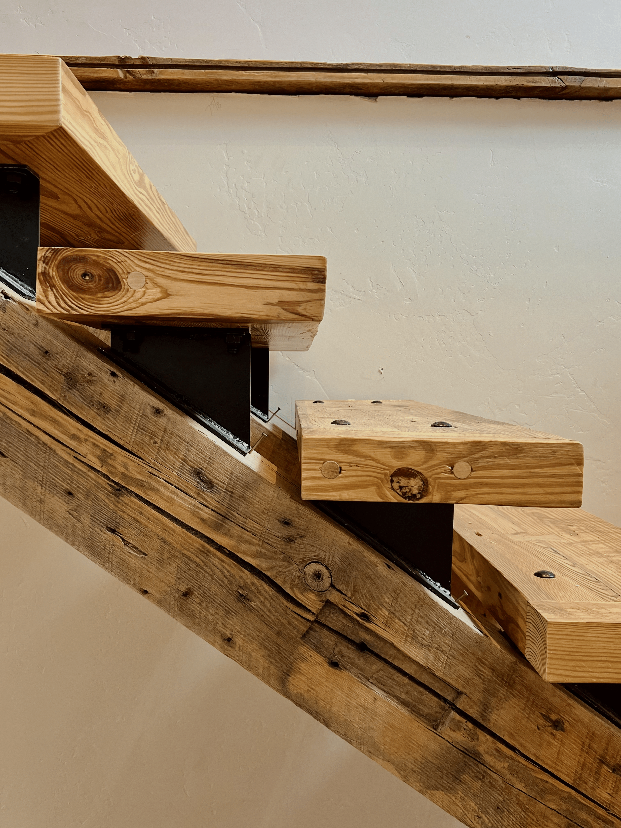Close-up of wooden staircase with visible grain and metal supports against a textured white wall.