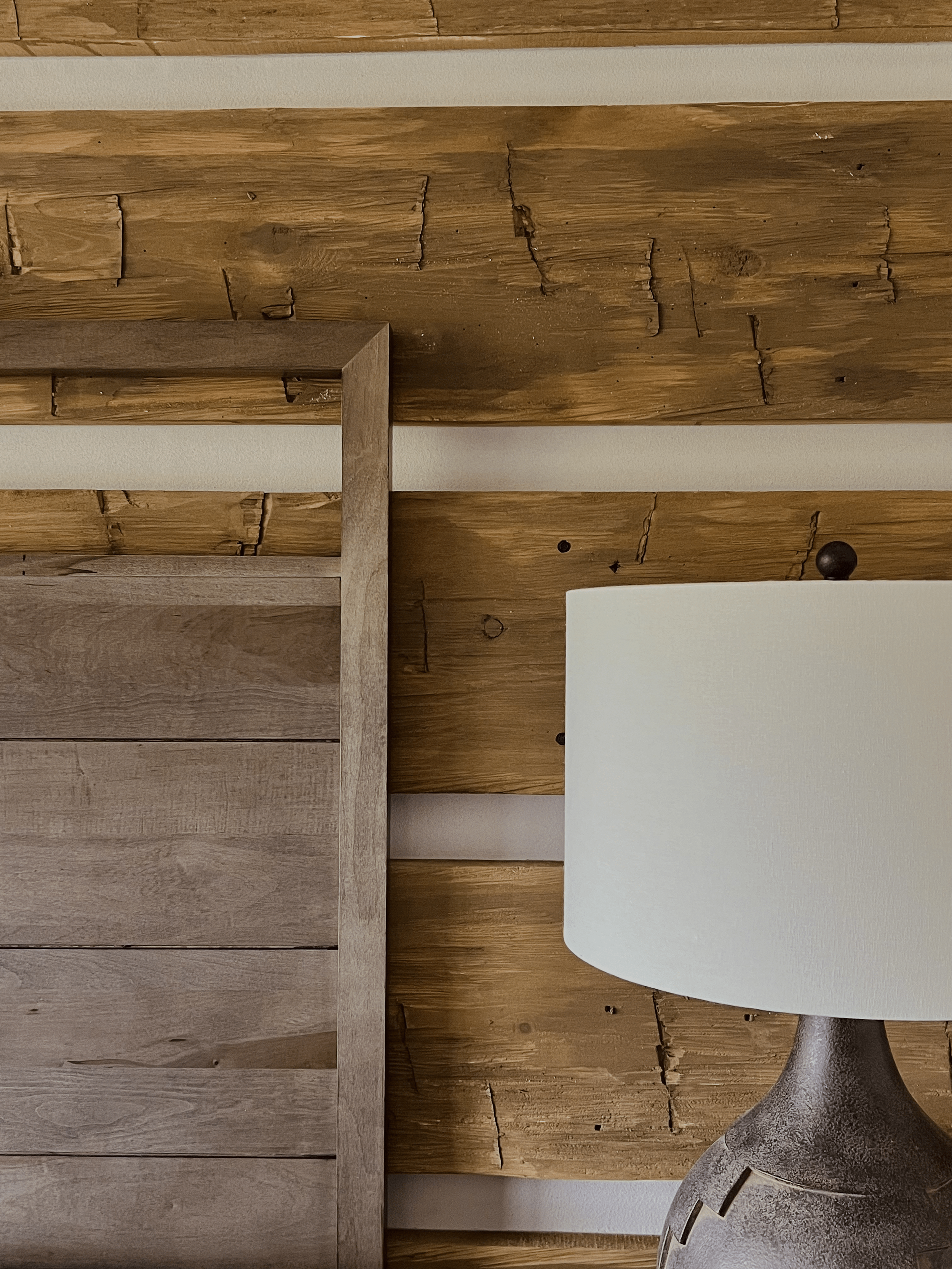 Close-up of a wooden headboard and a table lamp against a rustic wood-paneled wall.