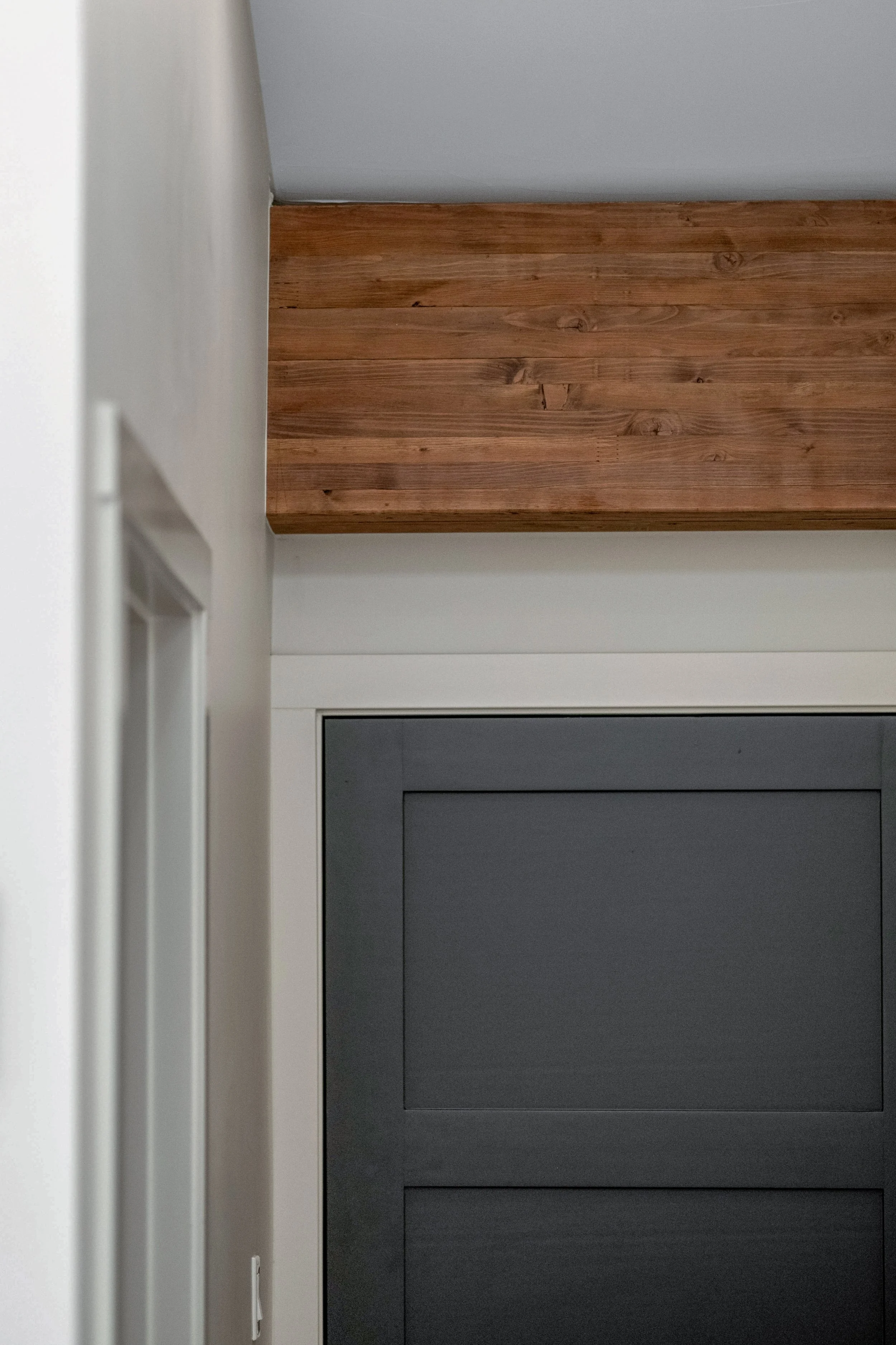 Close-up of a doorway with a gray door, white trim, and a wooden beam at the top.