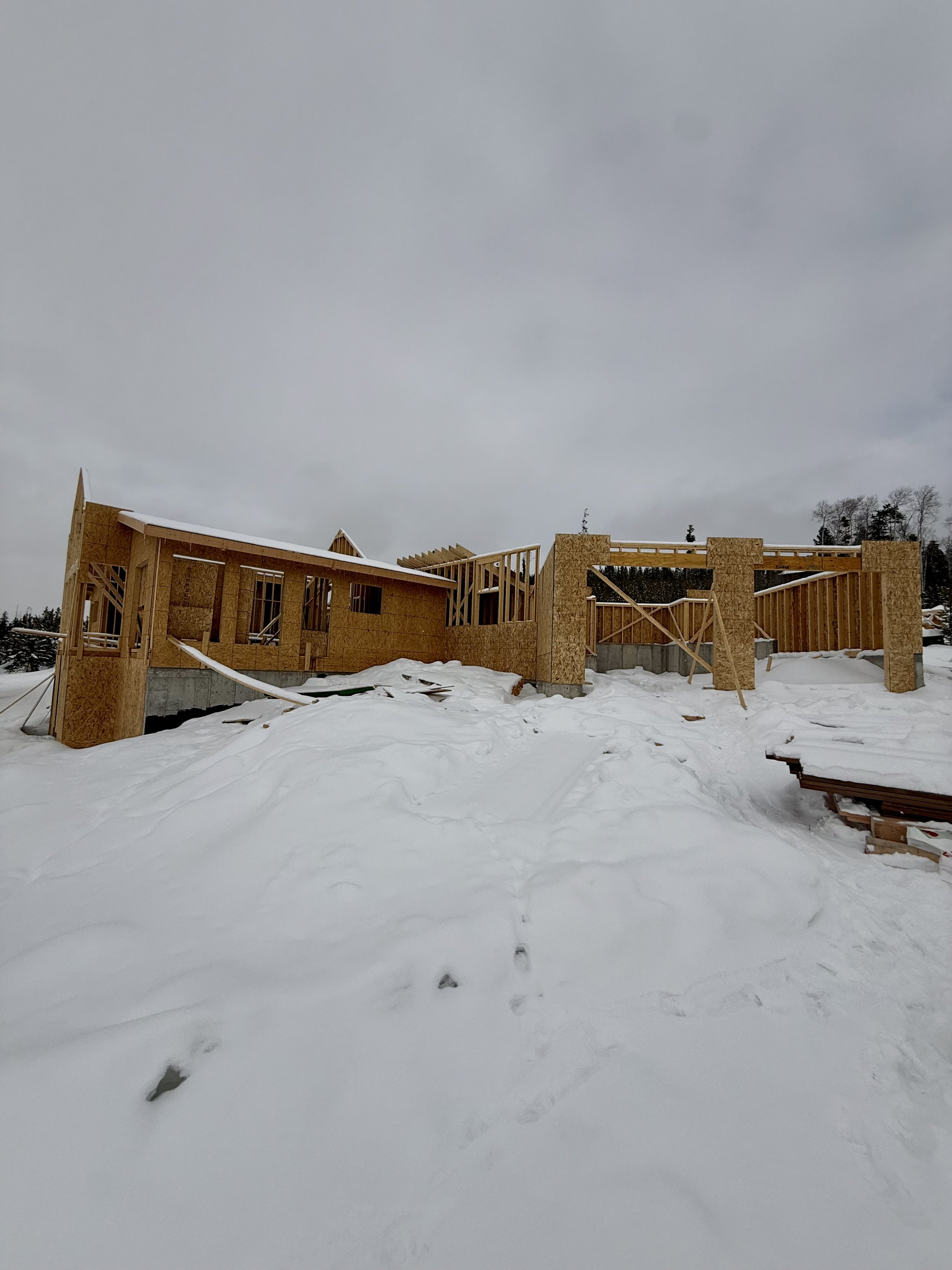Partially constructed house in snowy landscape with wooden framing visible.