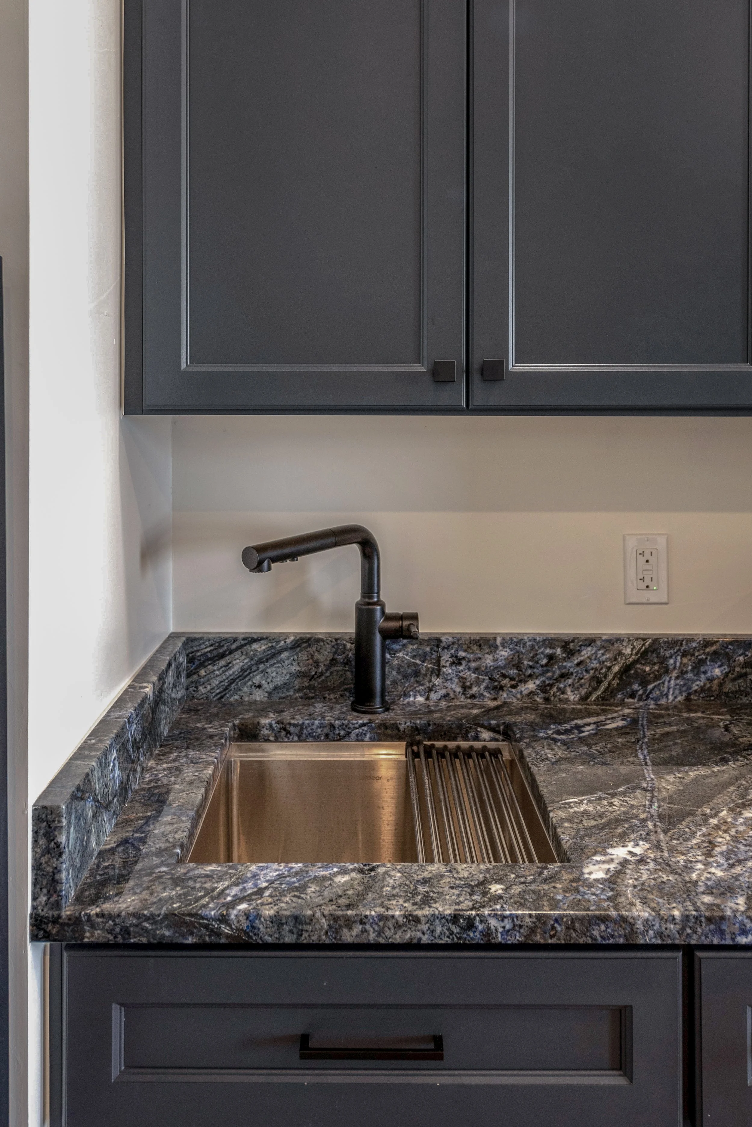 Modern kitchen sink with black faucet, granite countertop, and dark cabinets.