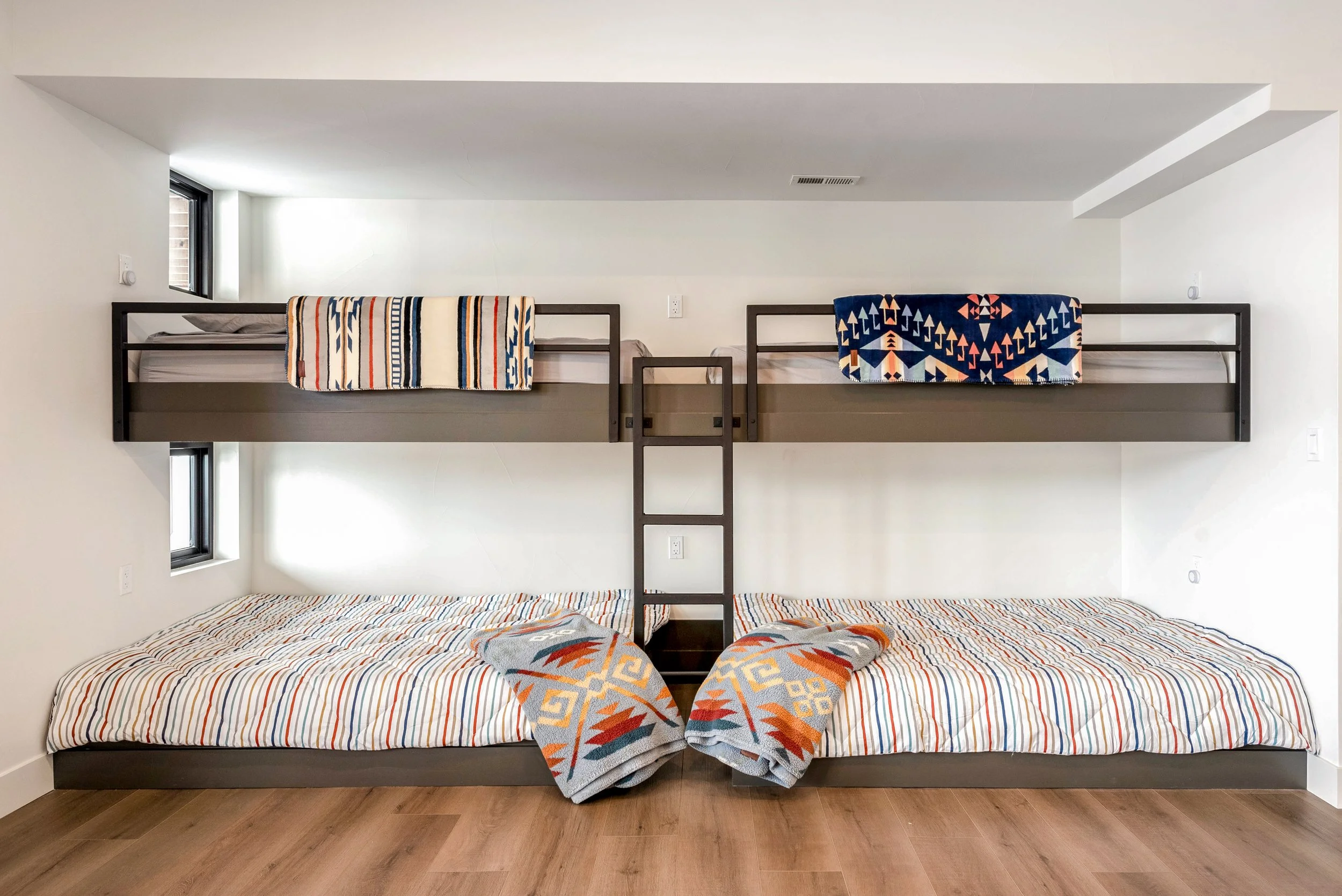 Bunk beds with patterned blankets and striated mattresses in a minimalist room.