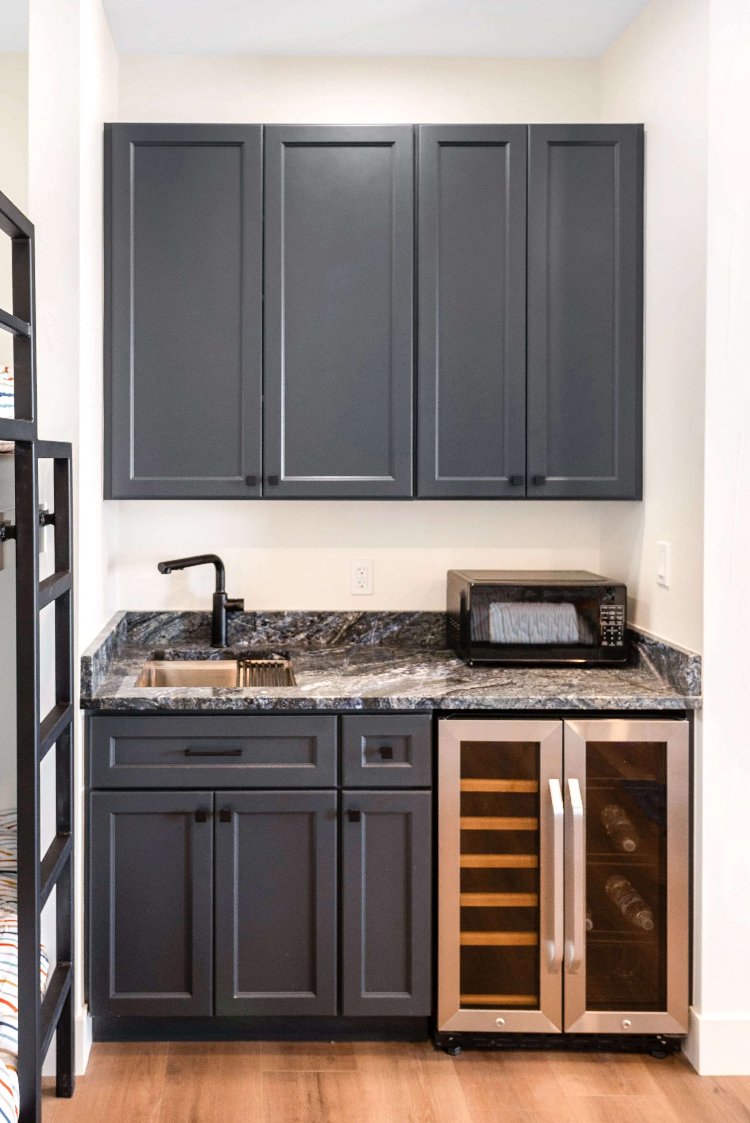Small kitchenette with dark grey cabinets, a black sink, a microwave, and a mini wine fridge.