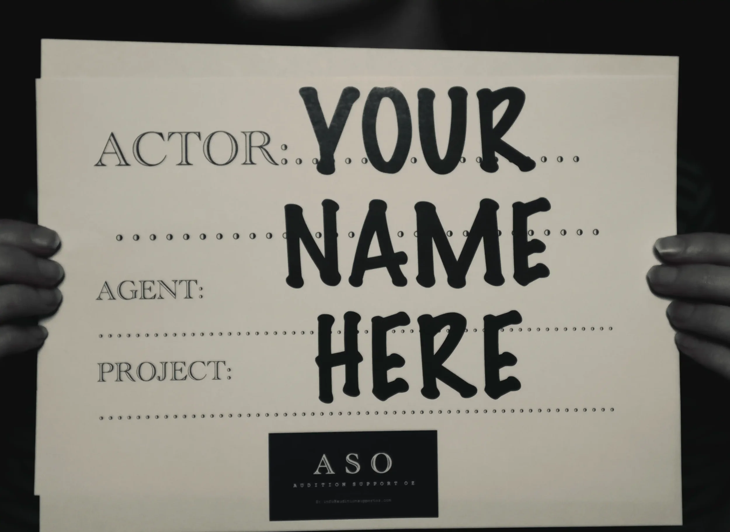 A paper casting slate being held to camera with the text "Your Name Here" drawn across it.