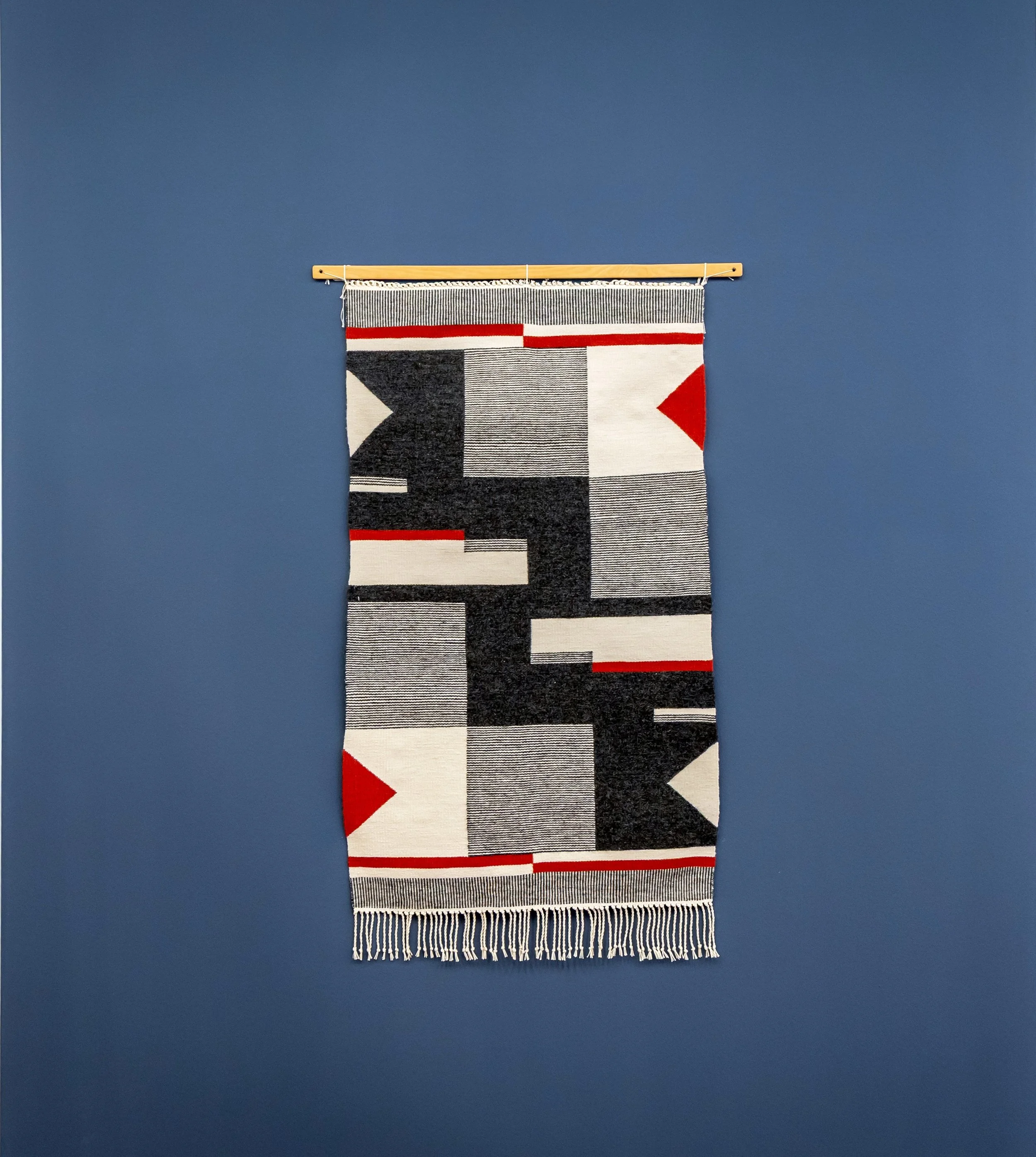 Häkelwandteppich mit geometrischem Muster in Schwarz, Weiß und Rot an blauer Wand