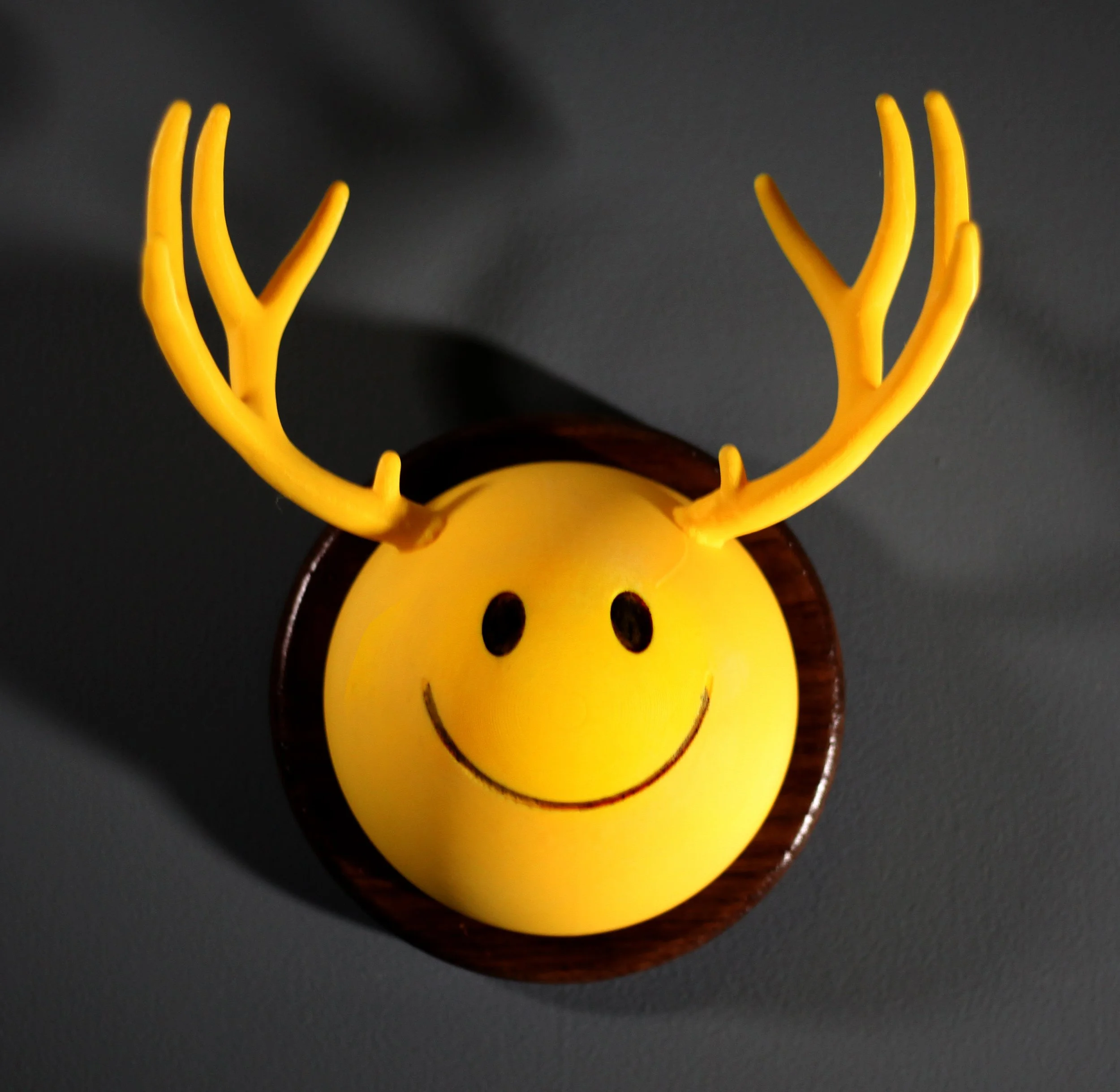 Yellow smiley face with antlers mounted on a wall